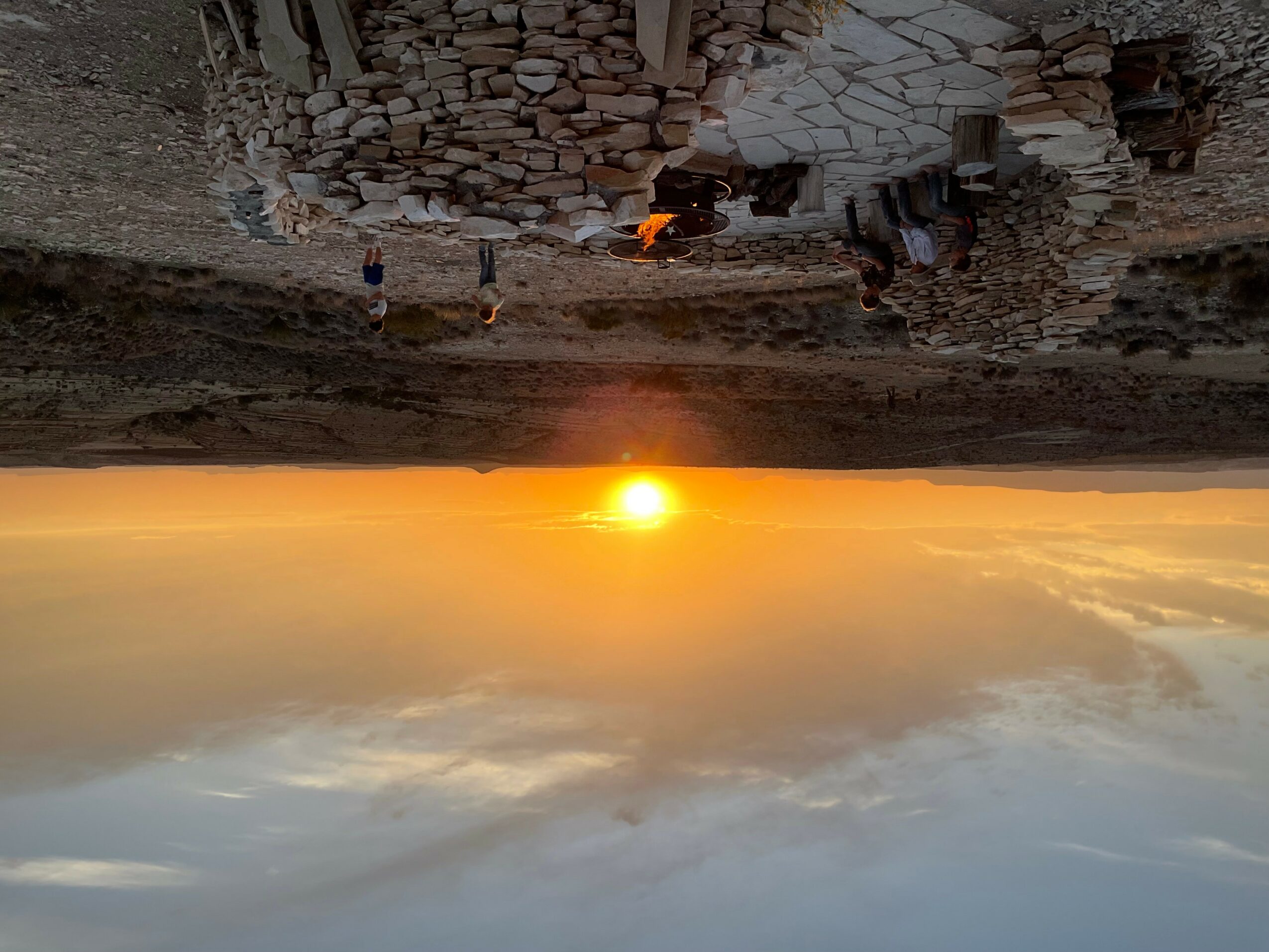 Sunset over a landscape with rocks and a small fire, with people in the distance, upside down.