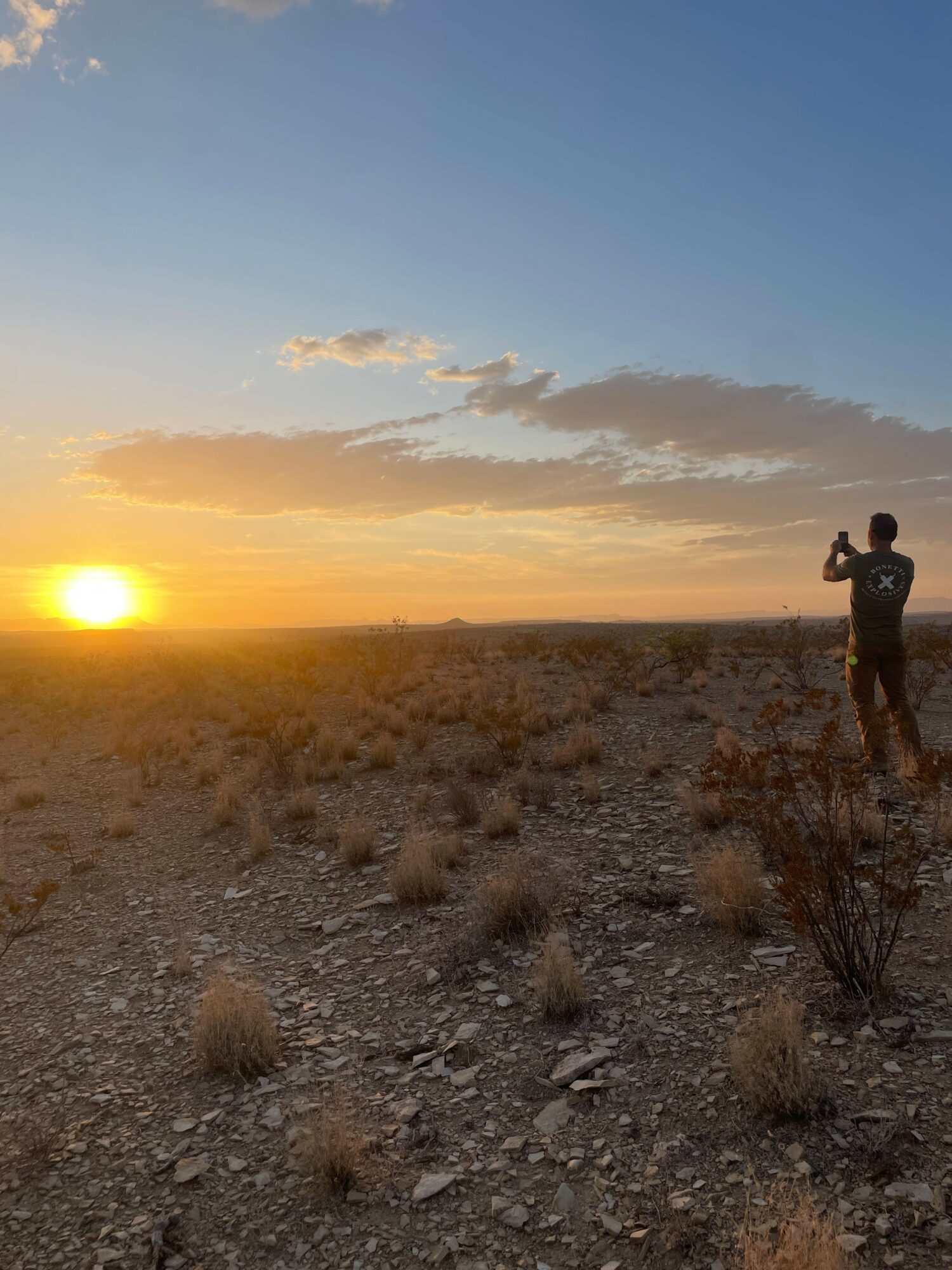 Person standing on rocky terrain during sunset with a colorful sky and clouds.