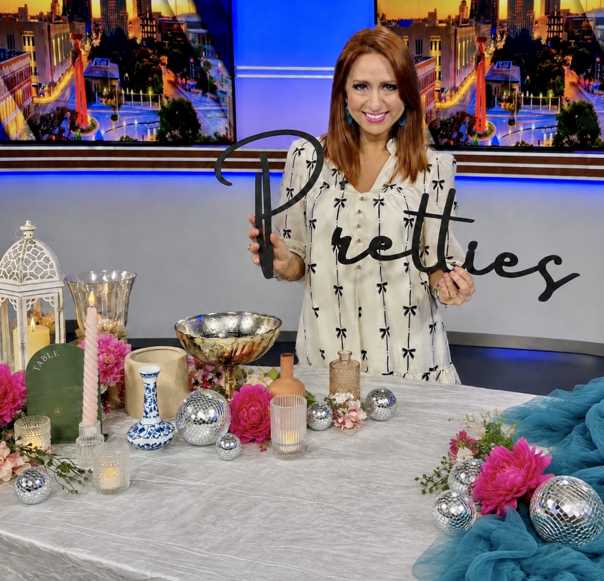 Woman with red hair smiling holding a sign that says 'Beautiful' behind a decorated table.