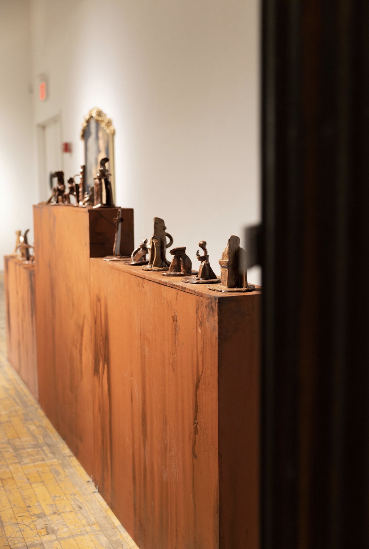 Wooden display shelf with small figurines, mirror on wall, and a white wall in the background.