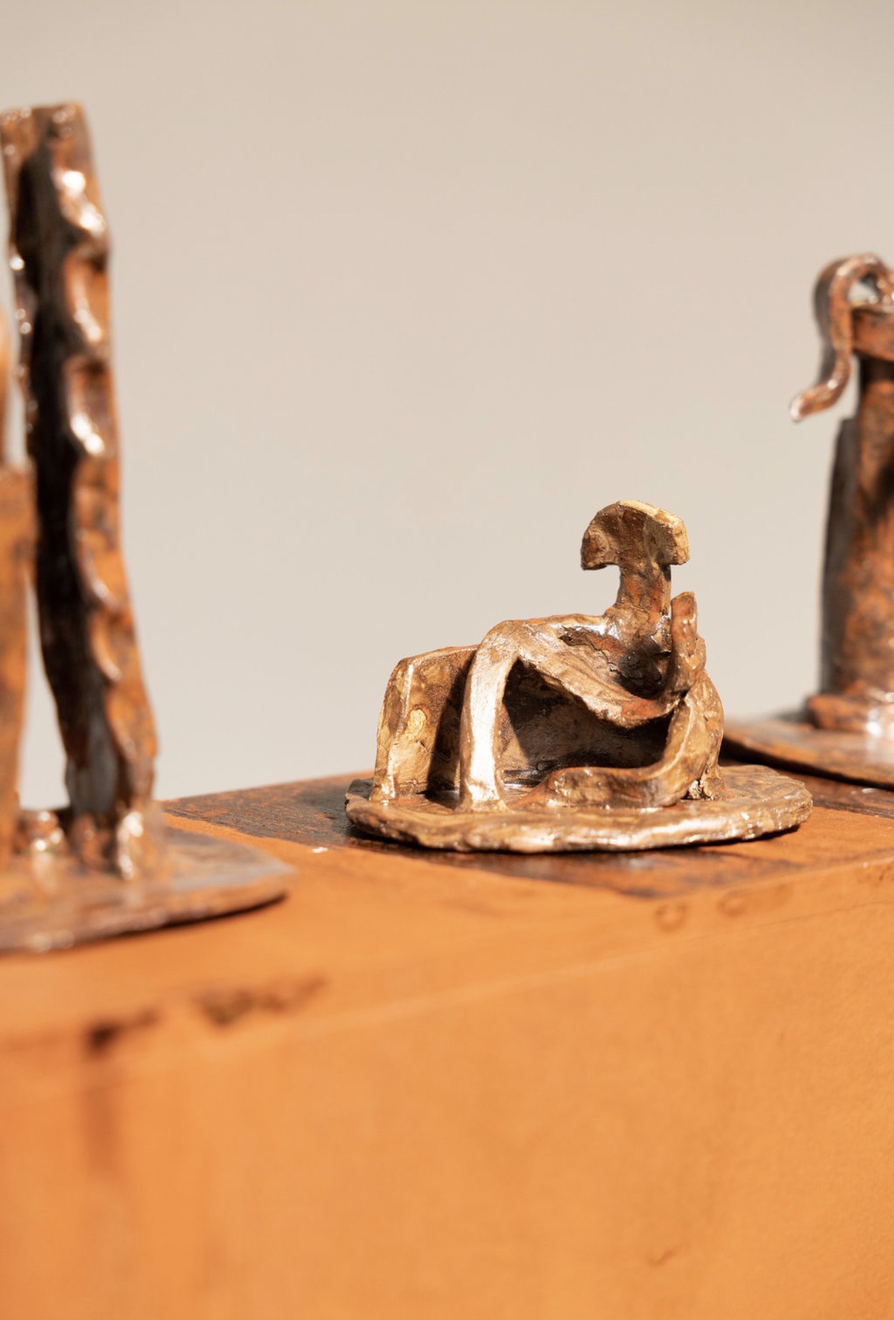 Close-up of a small, abstract sculpture of a seated figure with a rounded head, on a wooden surface.
