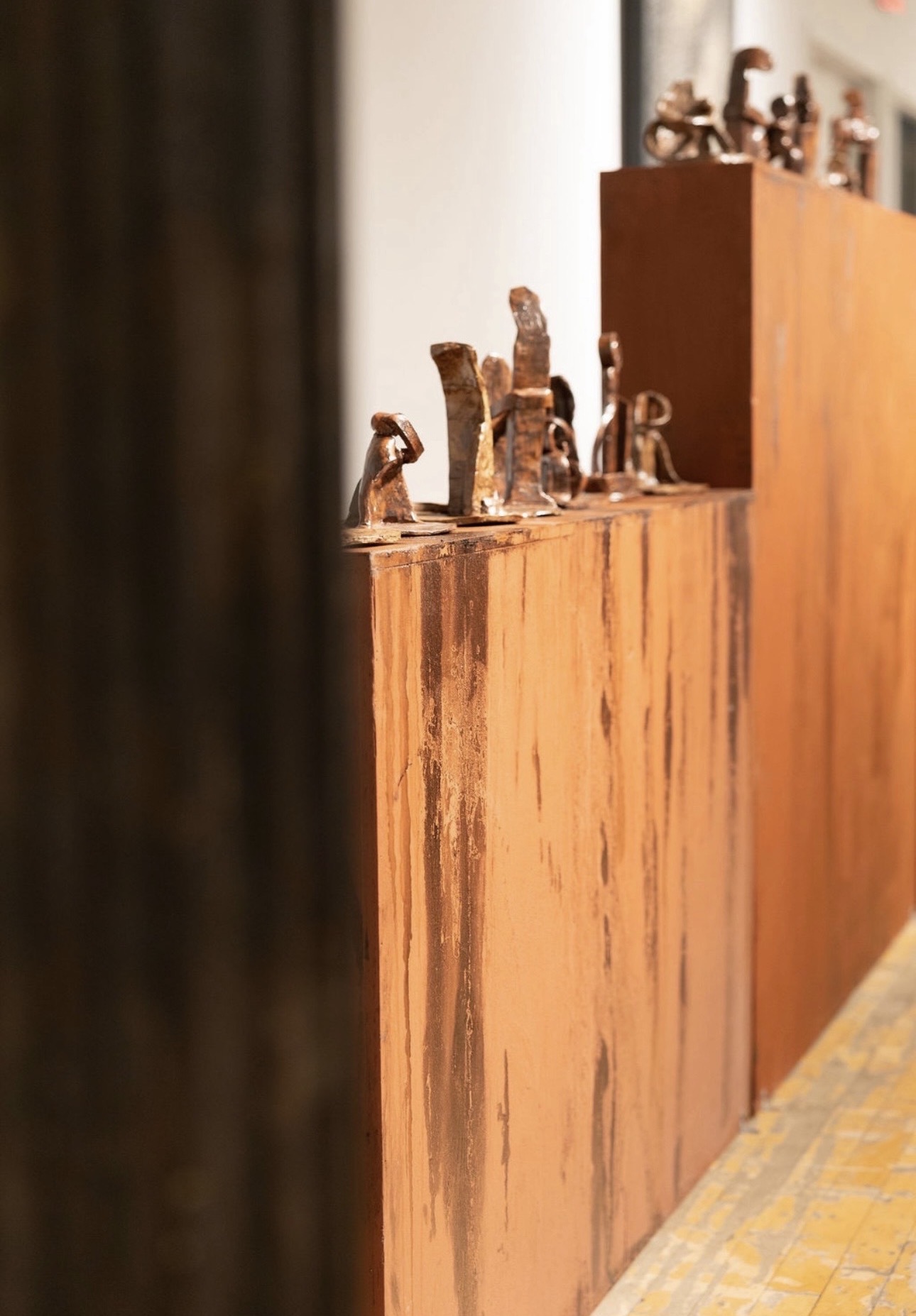 Wooden display with small animal figurines on top, against a background of a wooden cabinet and a tiled floor.