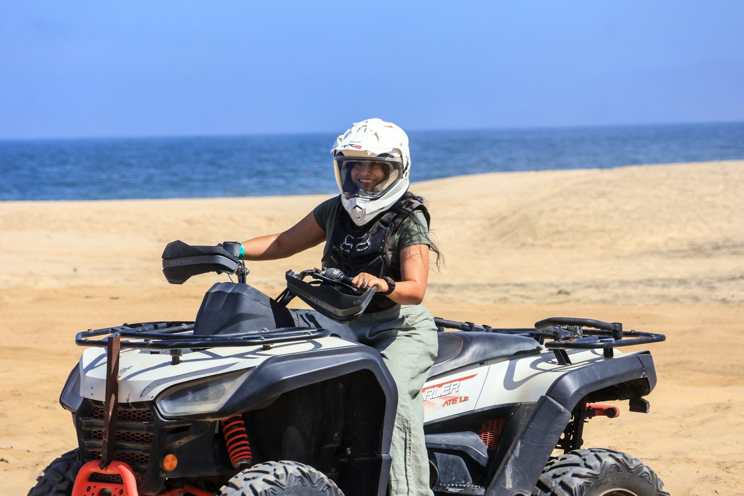 Child wearing a helmet riding an all-terrain vehicle on a sandy beach with ocean in background.