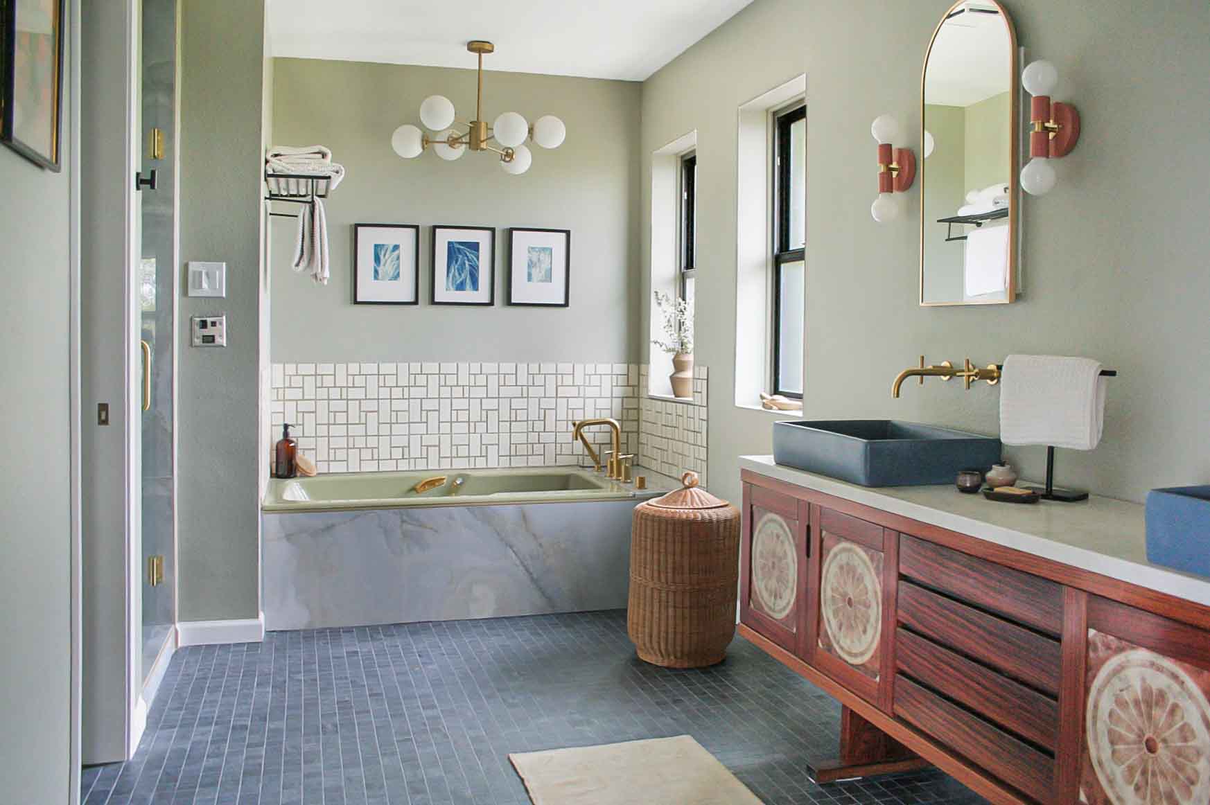 Bathroom with a bathtub, vanity with a sink, mirror, and decorative wall art, featuring light green walls and large windows.
