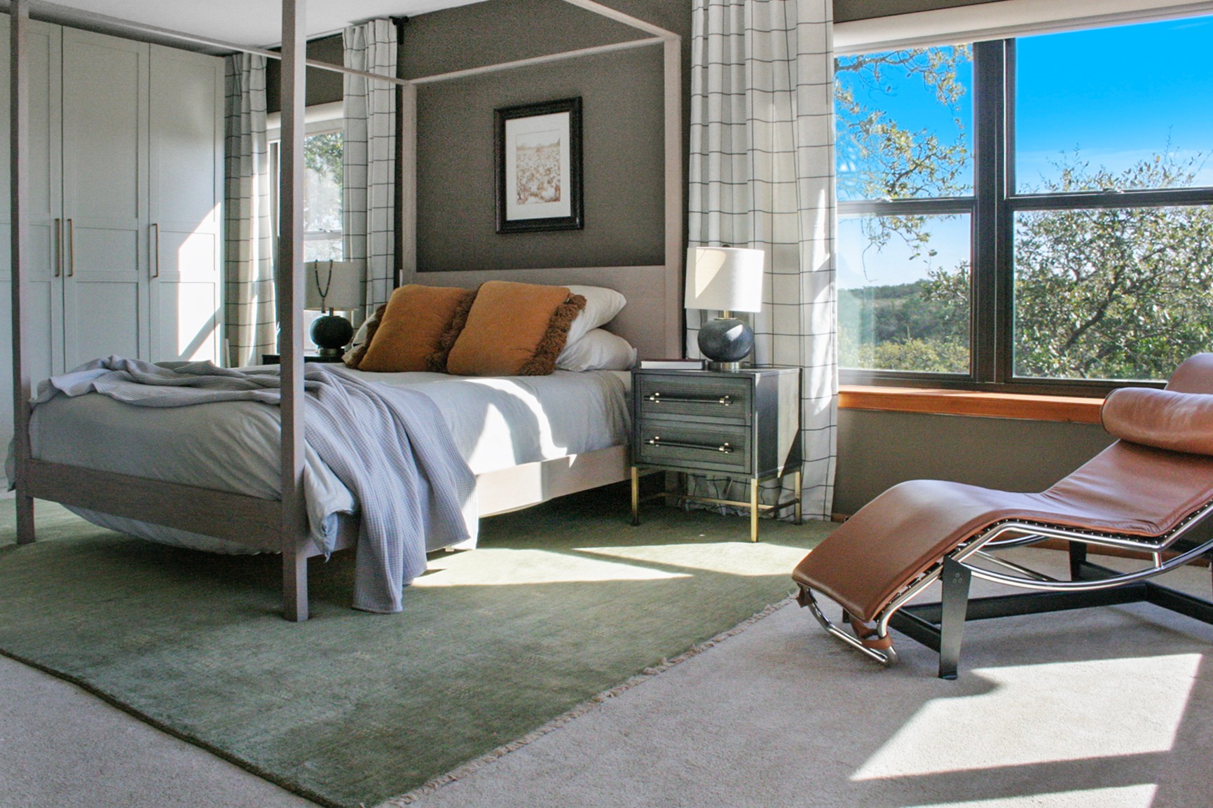 Bedroom with bed, nightstands, window, and lounge chair near window, sunlight streaming in, green outdoor view.
