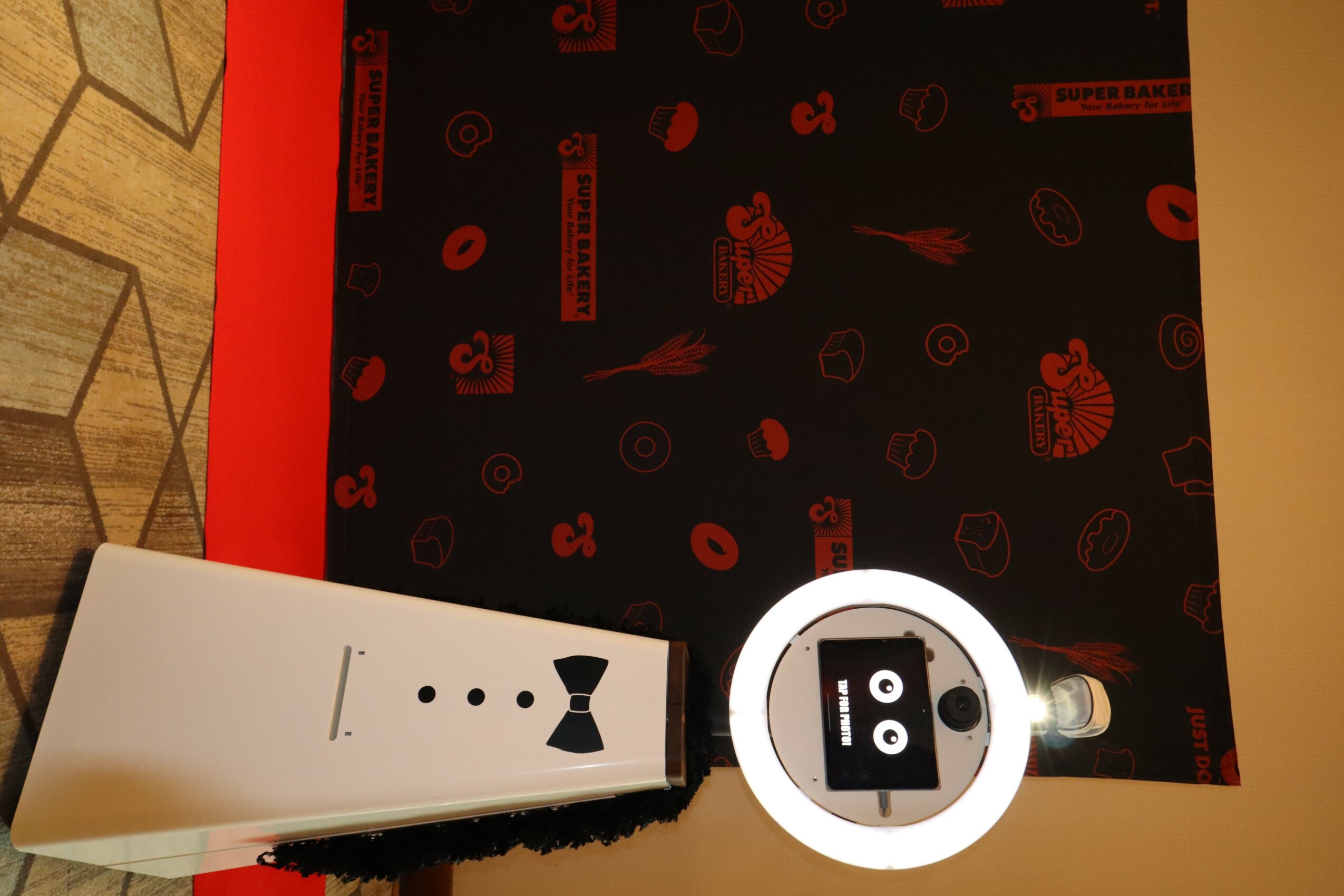 A white rectangular box with black dots and a bow tie illustration, placed on a surface with a black and red patterned background.