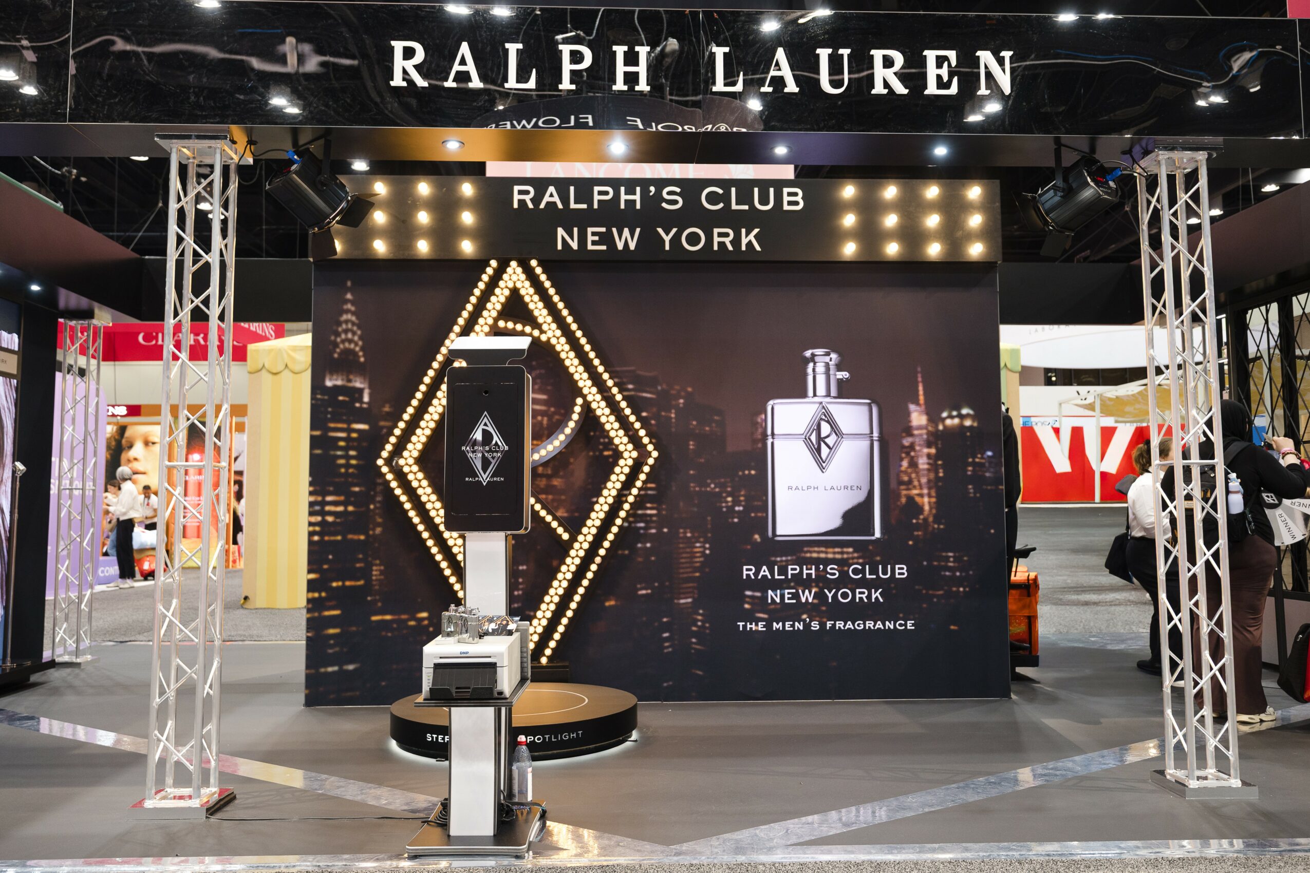 Ralph Lauren display with perfume bottles, black background, and gold accents, advertising Ralph's Club New York fragrance, in a shopping mall.
