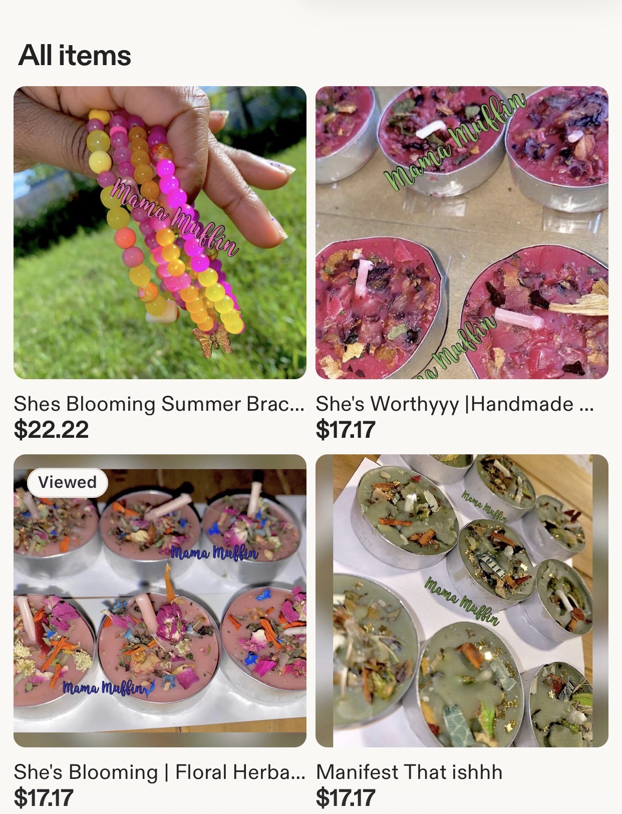 Hand holding colorful beaded jewelry, pink floral candles, and herbal manifest items on a table.