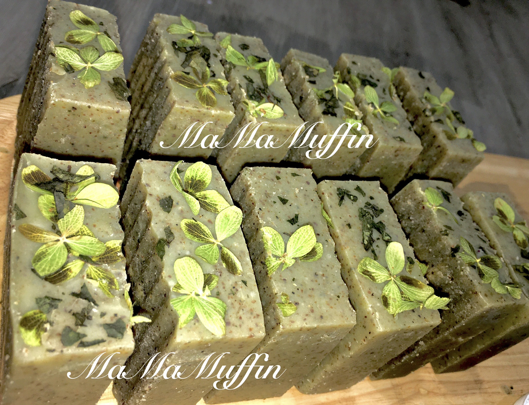Rows of rectangular greenish soap bars decorated with mint leaves, arranged on a wooden surface.