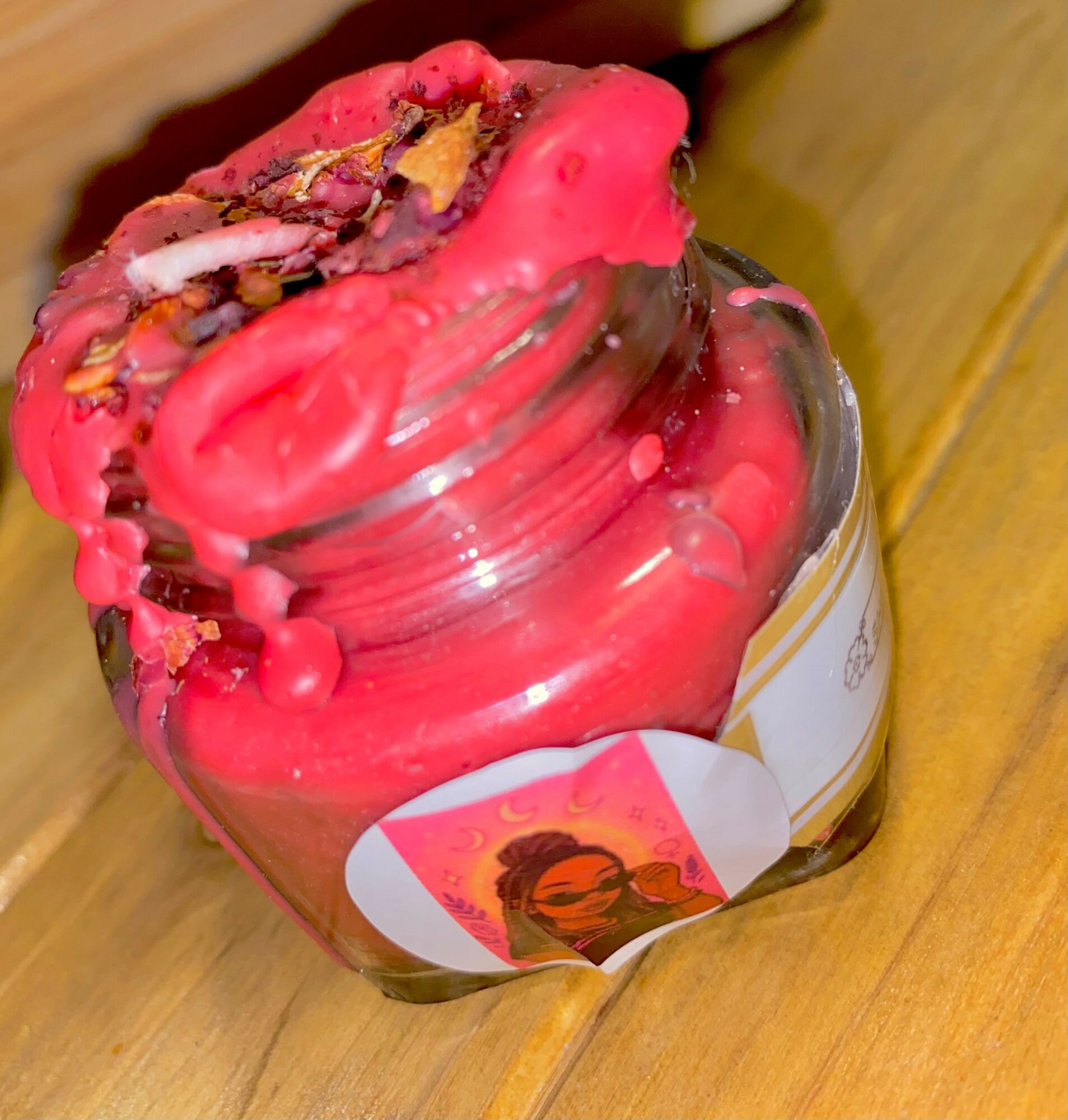 Open jar with pink and multicolored sprinkles on top, placed on a wooden surface.