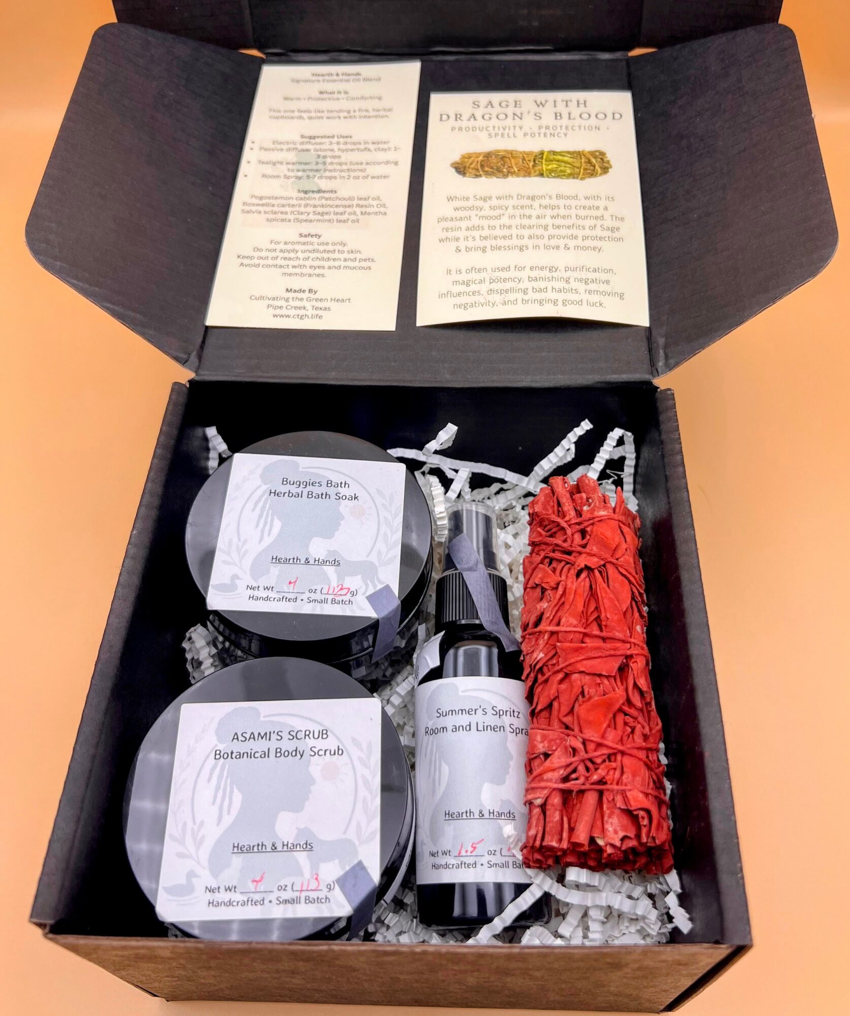Open black box with red rolled item, two containers, and papers inside, on a peach-colored surface.
