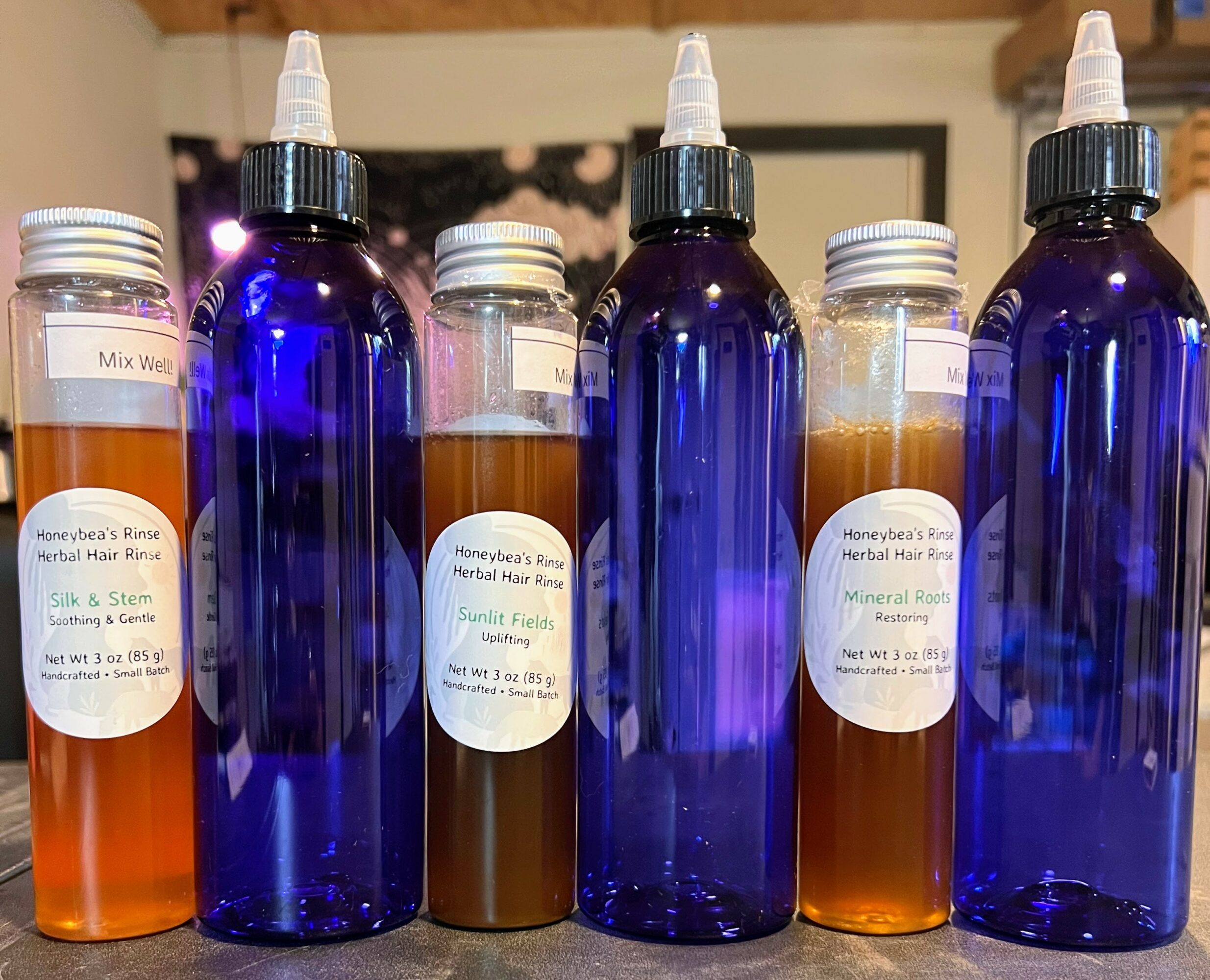 Six bottles, three blue with white caps, two clear with orange liquid, one orange with white cap, on a countertop.
