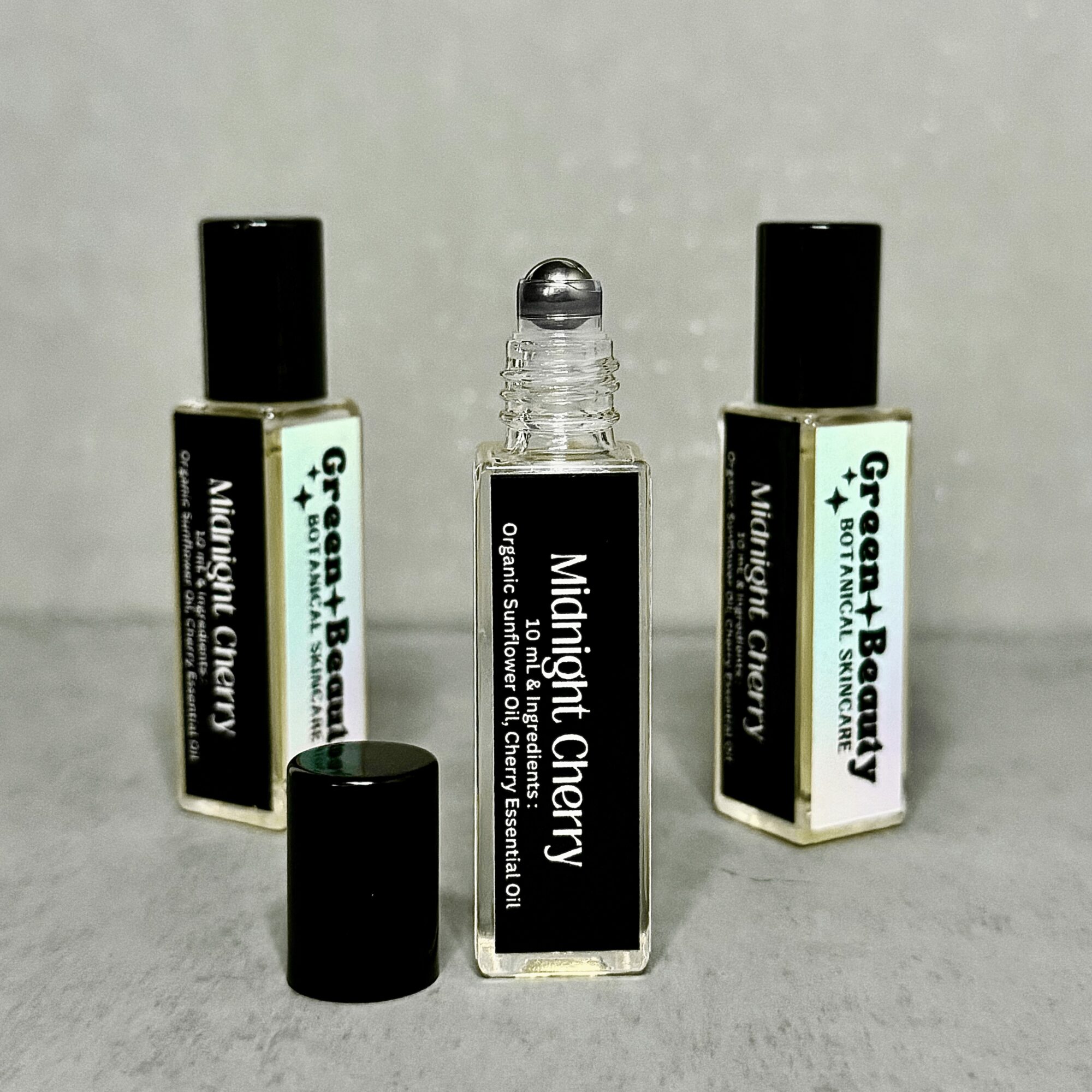 Three small bottles with black caps, one with a label reading 'Midnight Cherry', on a gray background.