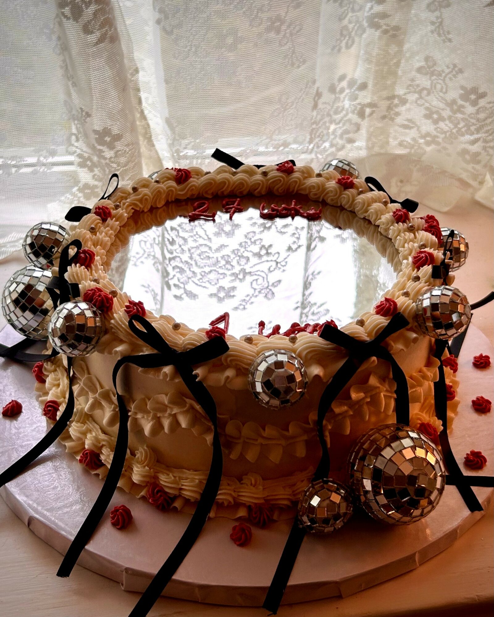Decorative headband with small disco balls, black ribbons, and red accents, placed on a pink surface with scattered red beads.