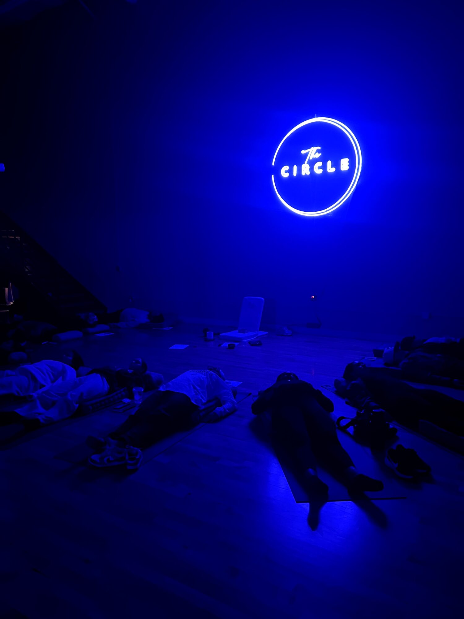 Neon sign reading 'CIRCLES' inside a circle, glowing blue against a dark background, with scattered objects on the floor.
