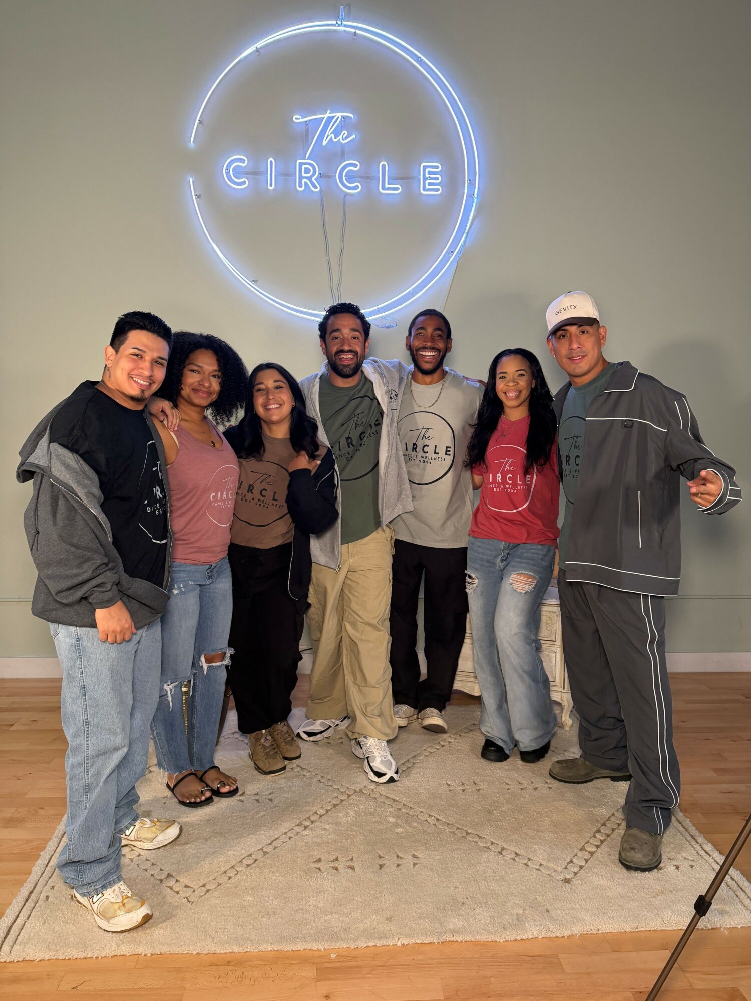 Group of seven people standing indoors, with a neon sign reading 'CIRCLE' on the wall behind them.