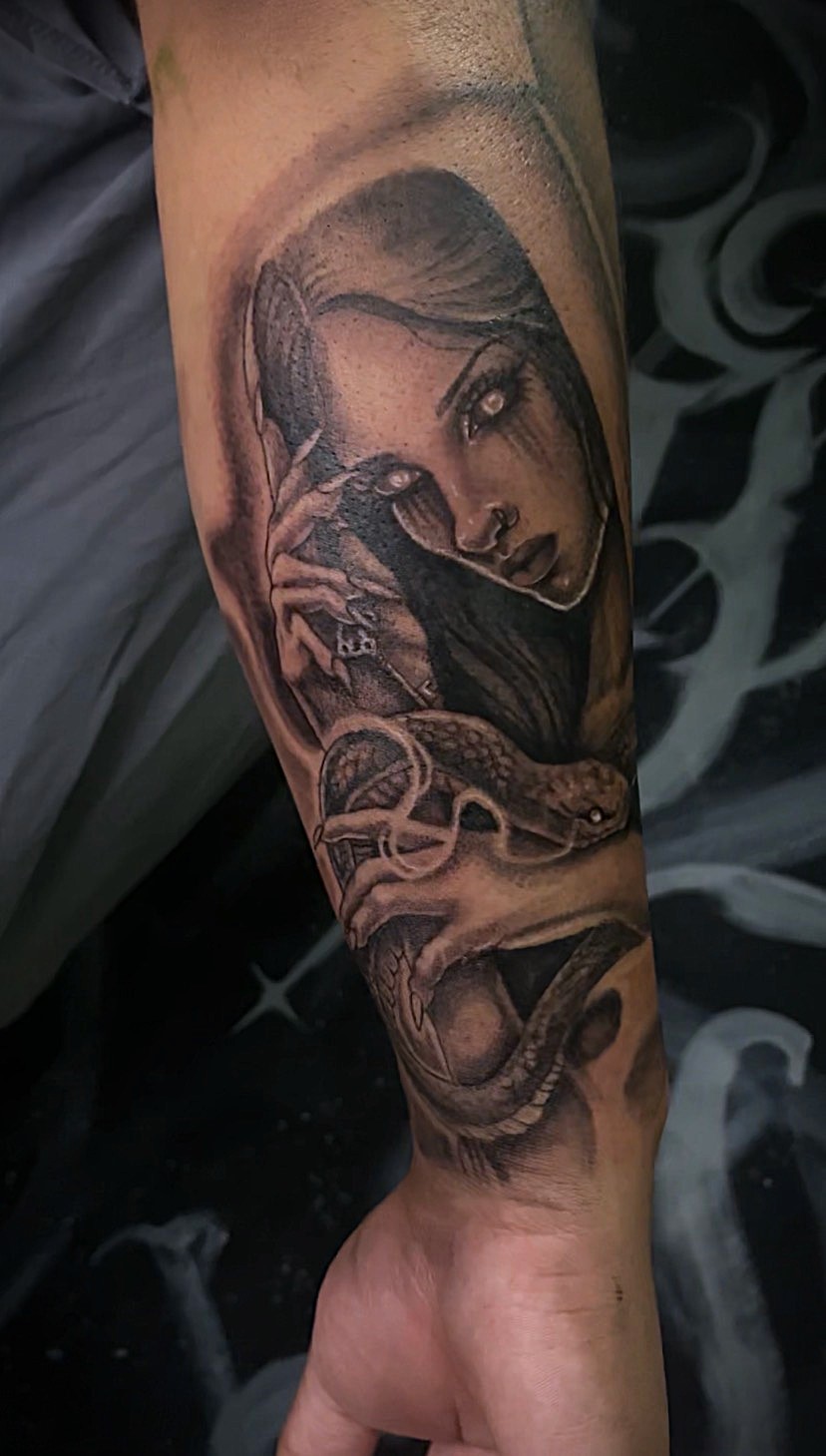Tattoo of a woman with long hair, holding a snake near her face, with detailed shading and realistic style.