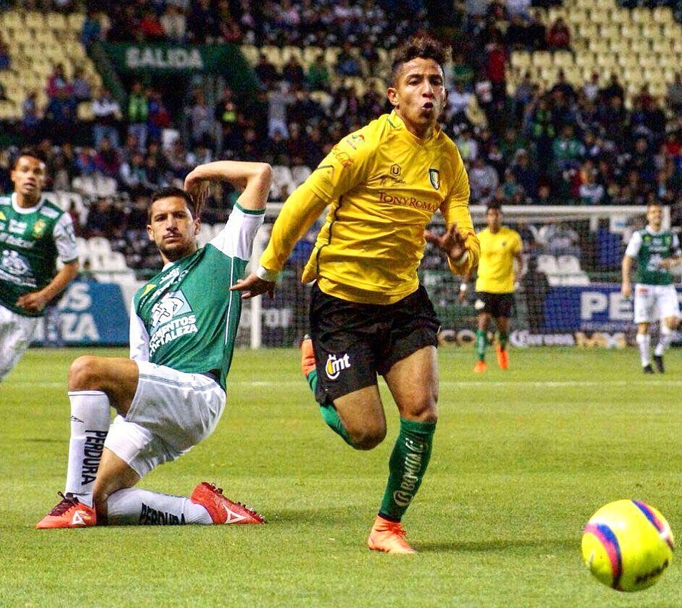 Two soccer players on the field, one in yellow running, the other in green sliding, with a colorful ball nearby.