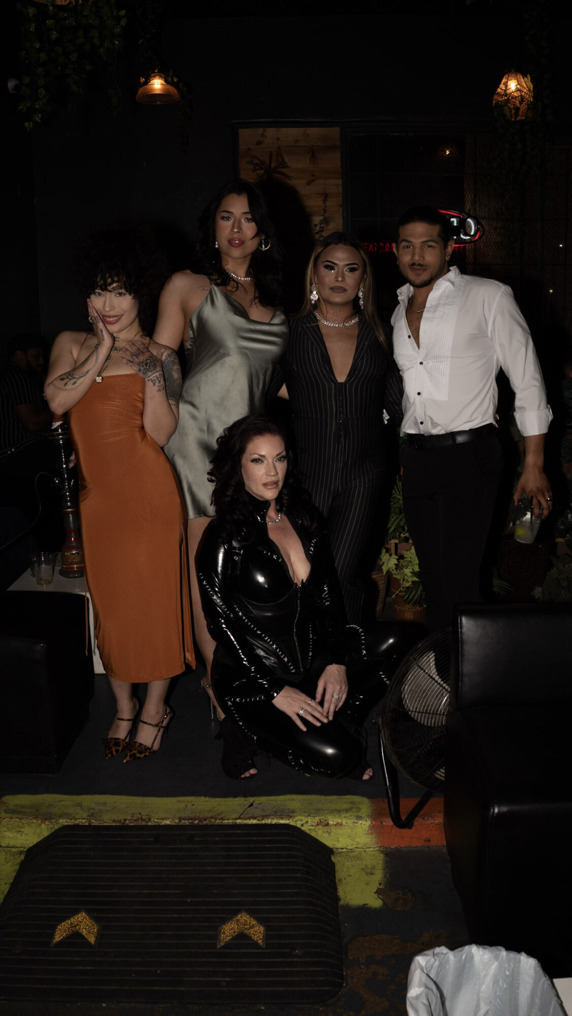 Group of five women posing indoors, some standing and one sitting, dressed in formal and stylish clothing.