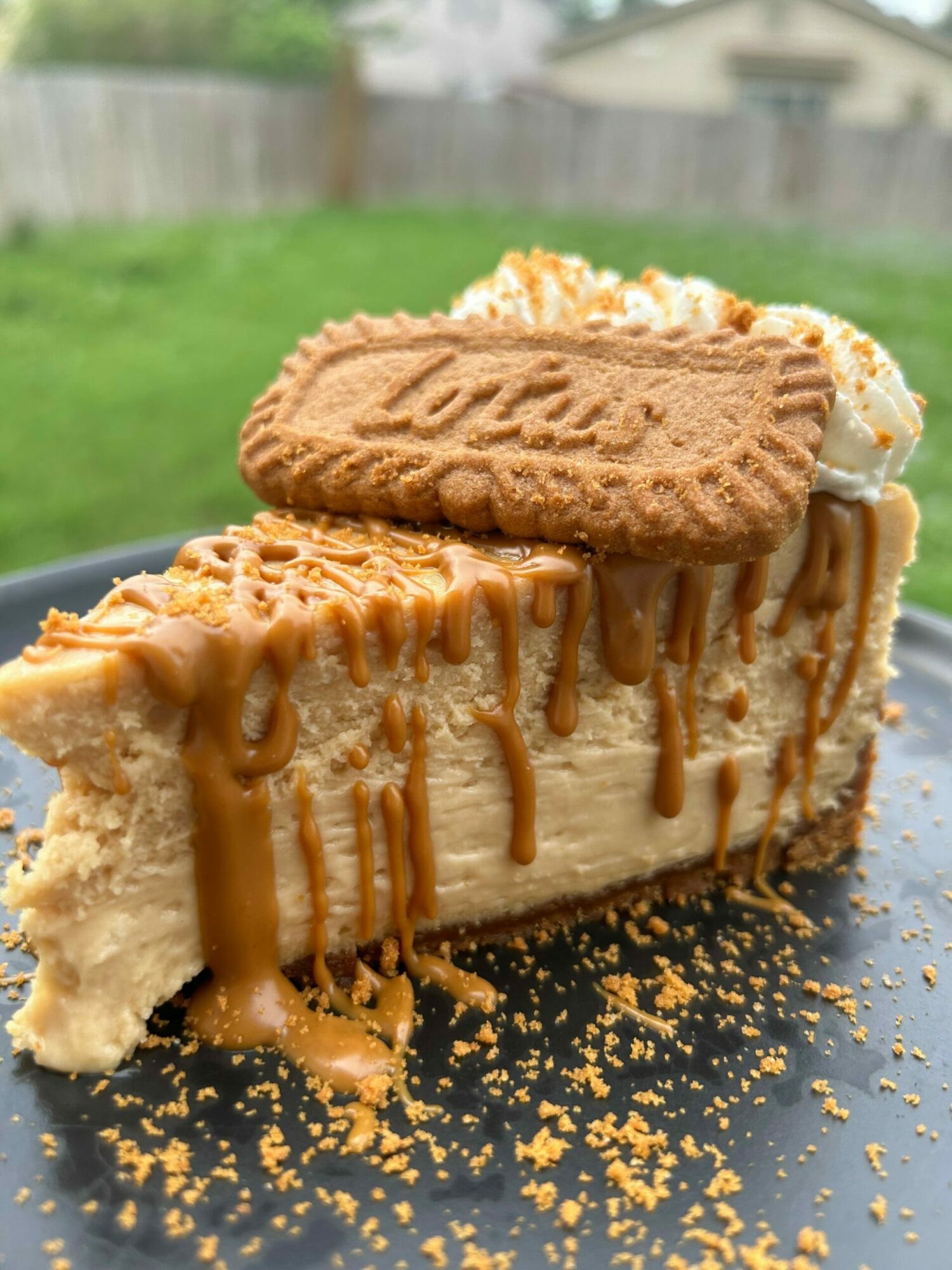 Slice of ice cream cake with cookies and caramel drizzle on black plate, crumbs scattered around.