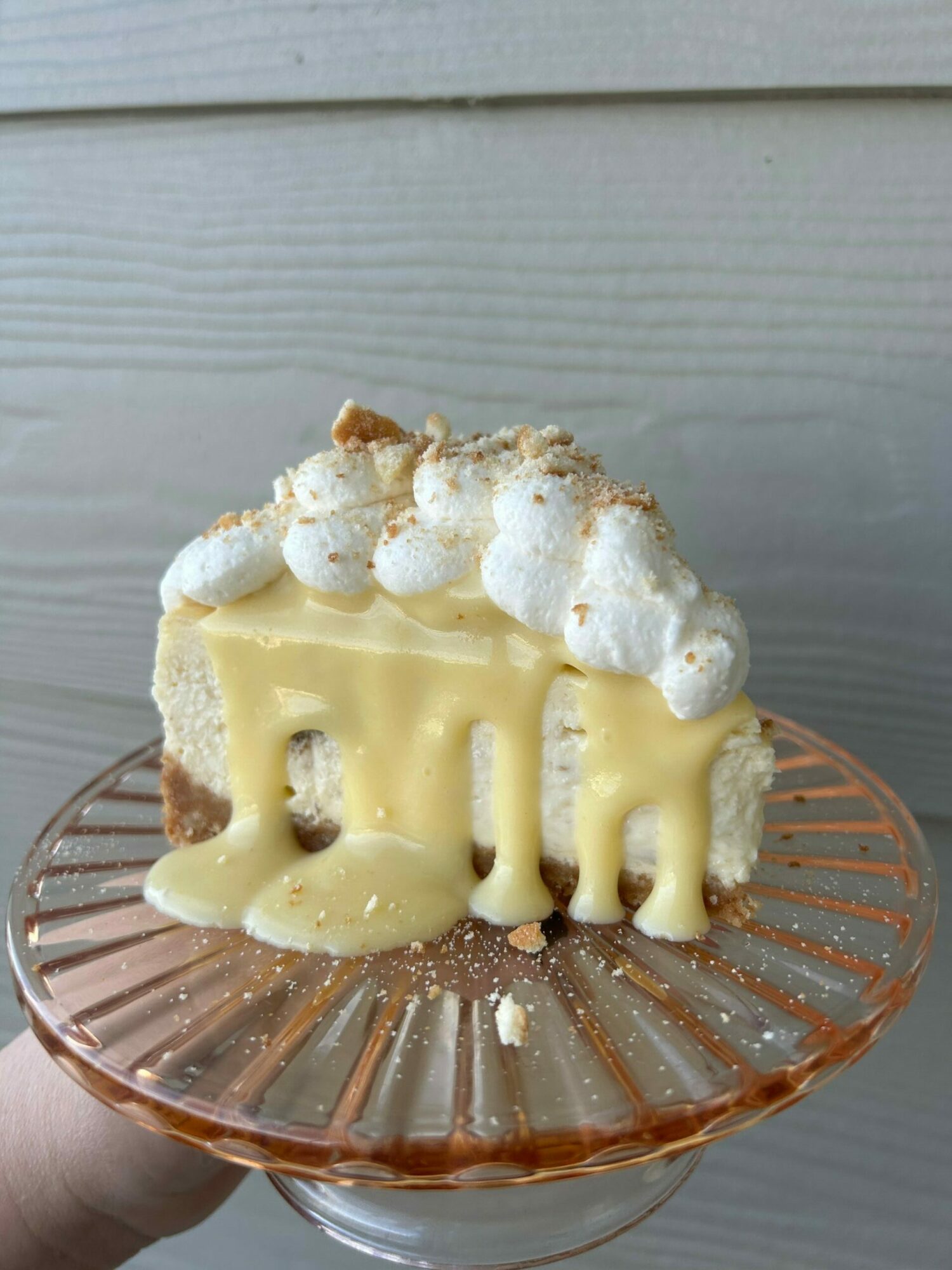 Dessert with whipped cream, white chocolate, and a biscuit on a pink glass plate, held by a hand.