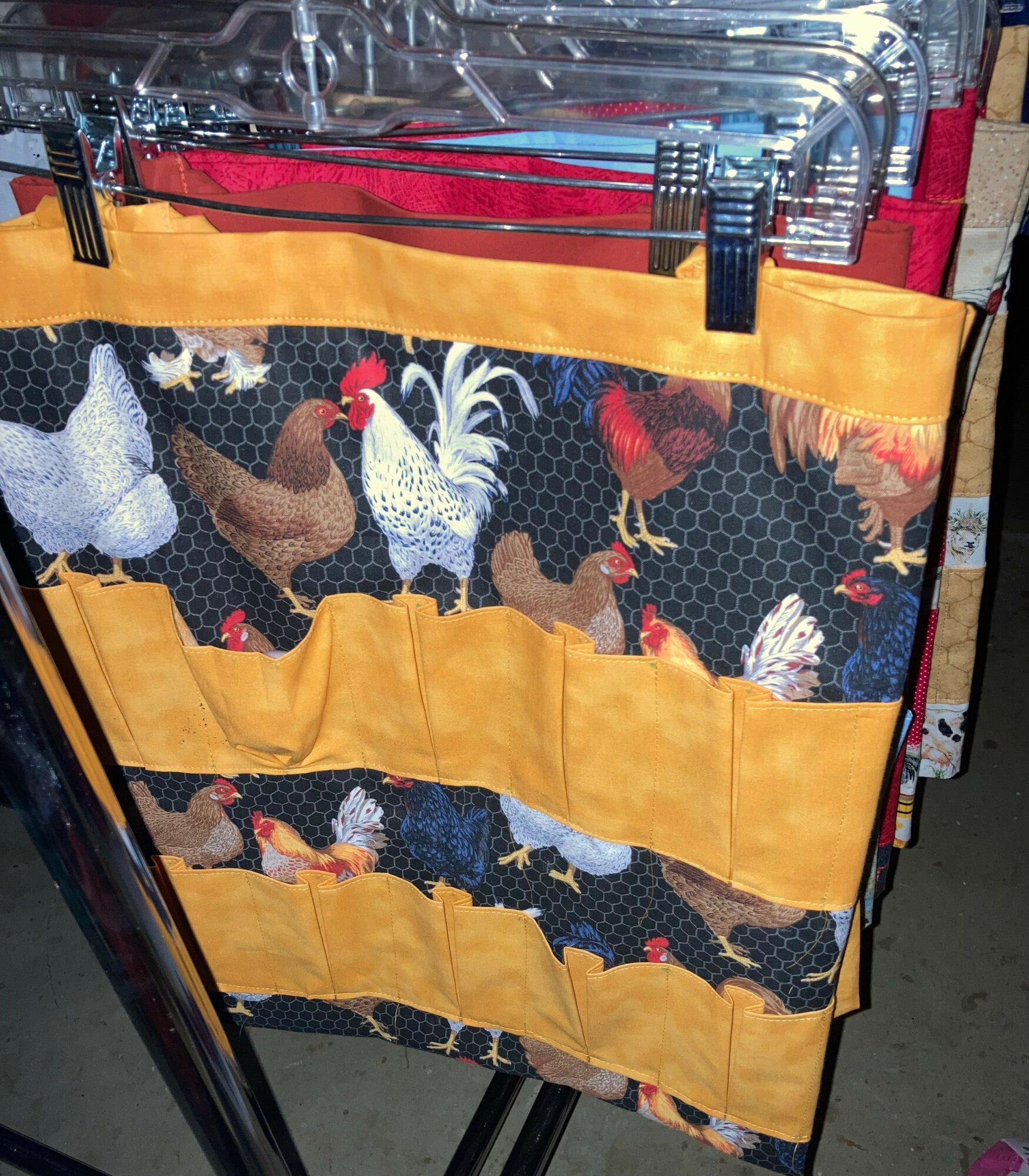 Fabric organizer with chicken and rooster pattern, multiple pockets, hanging on a metal rack, with a yellow top edge.