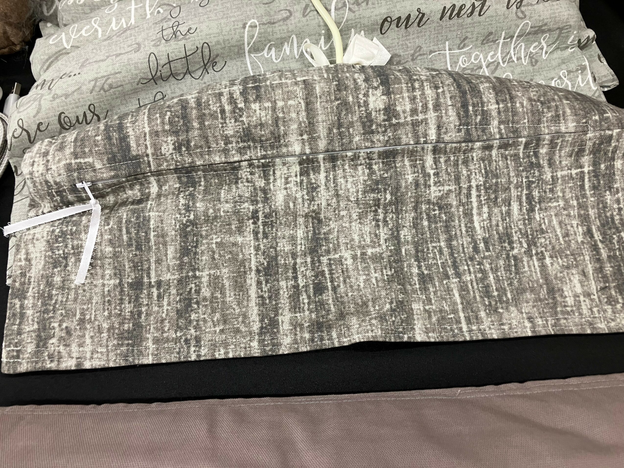 Close-up of a fabric pillow with a textured gray and white pattern, resting on a bed with printed sheets.