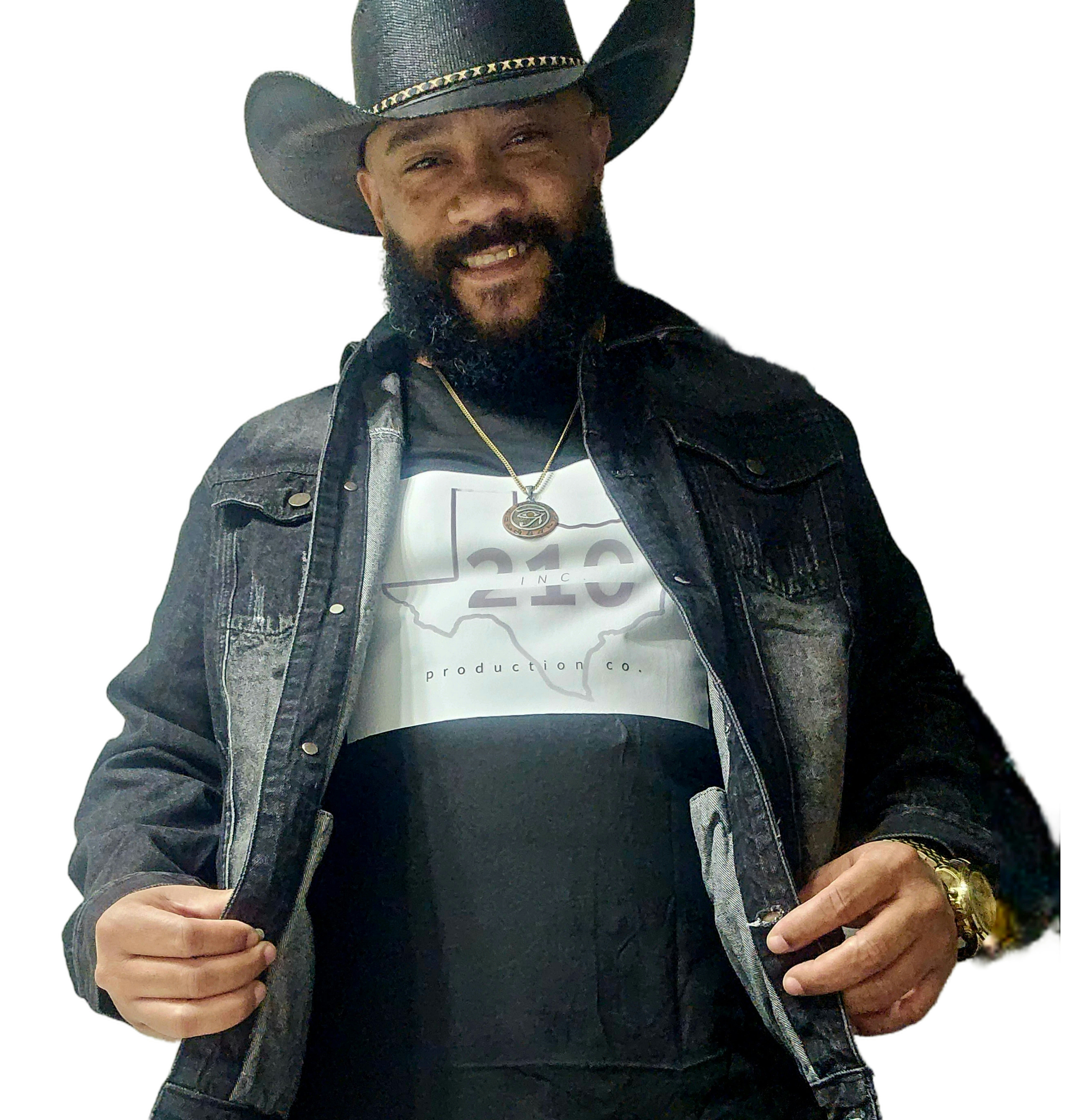 Man with a beard wearing a cowboy hat, denim jacket, and white shirt, smiling, holding the jacket open, against a white background.