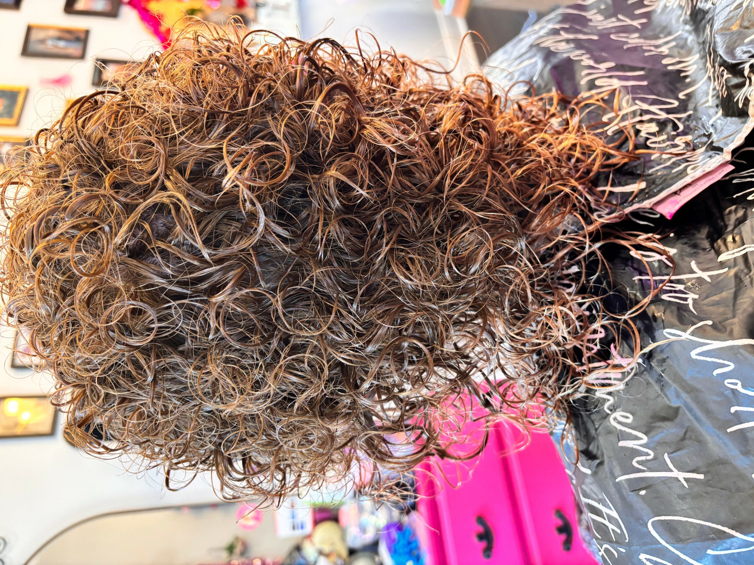 Close-up of curly hair with various shades of brown and blonde, styled in tight ringlets.
