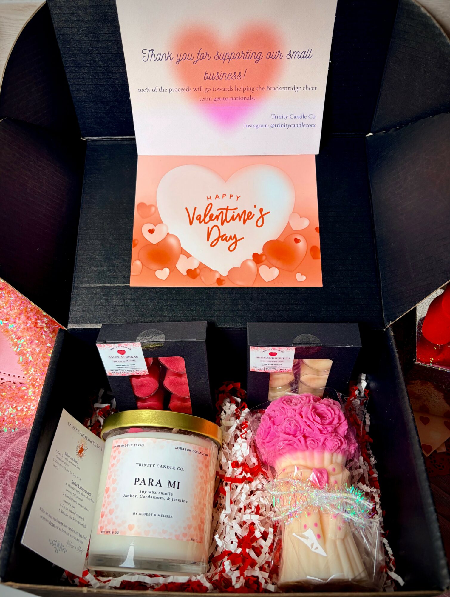 Open gift box with Valentine's Day themed card, candle, pink yarn, and wrapped treats inside.