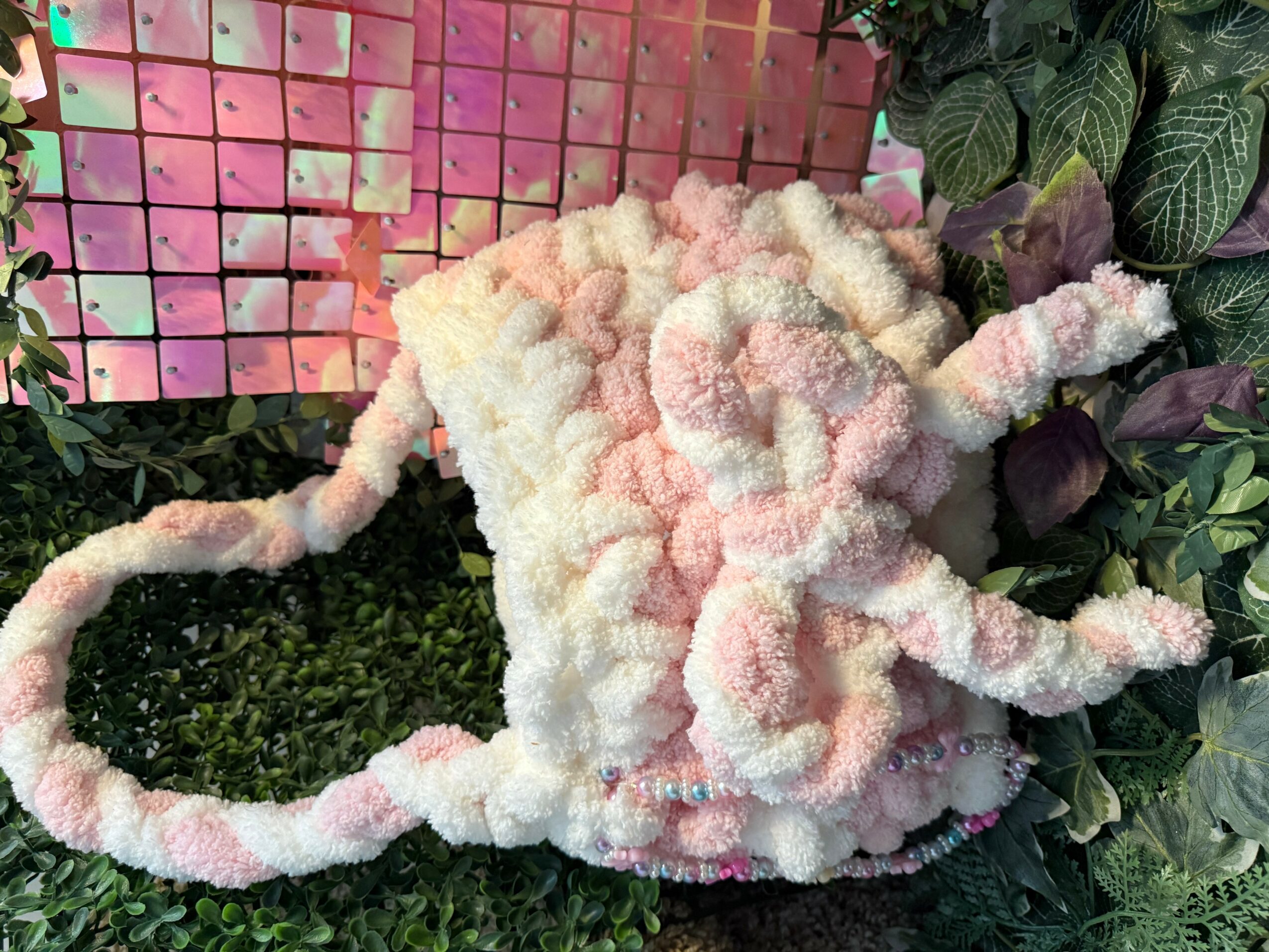 Soft, fluffy bag with pink and white colors, surrounded by green and purple leaves, and a colorful background.