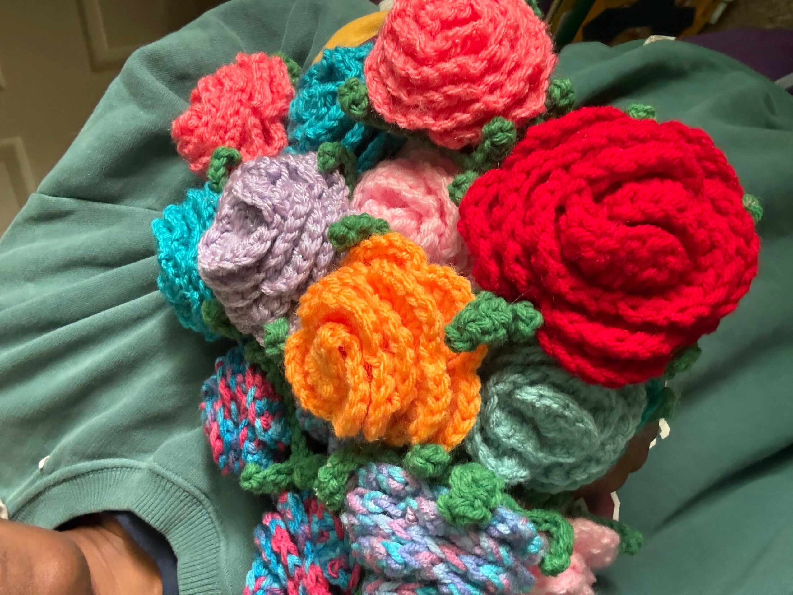 Colorful crocheted flowers and roses arranged on a green fabric surface.