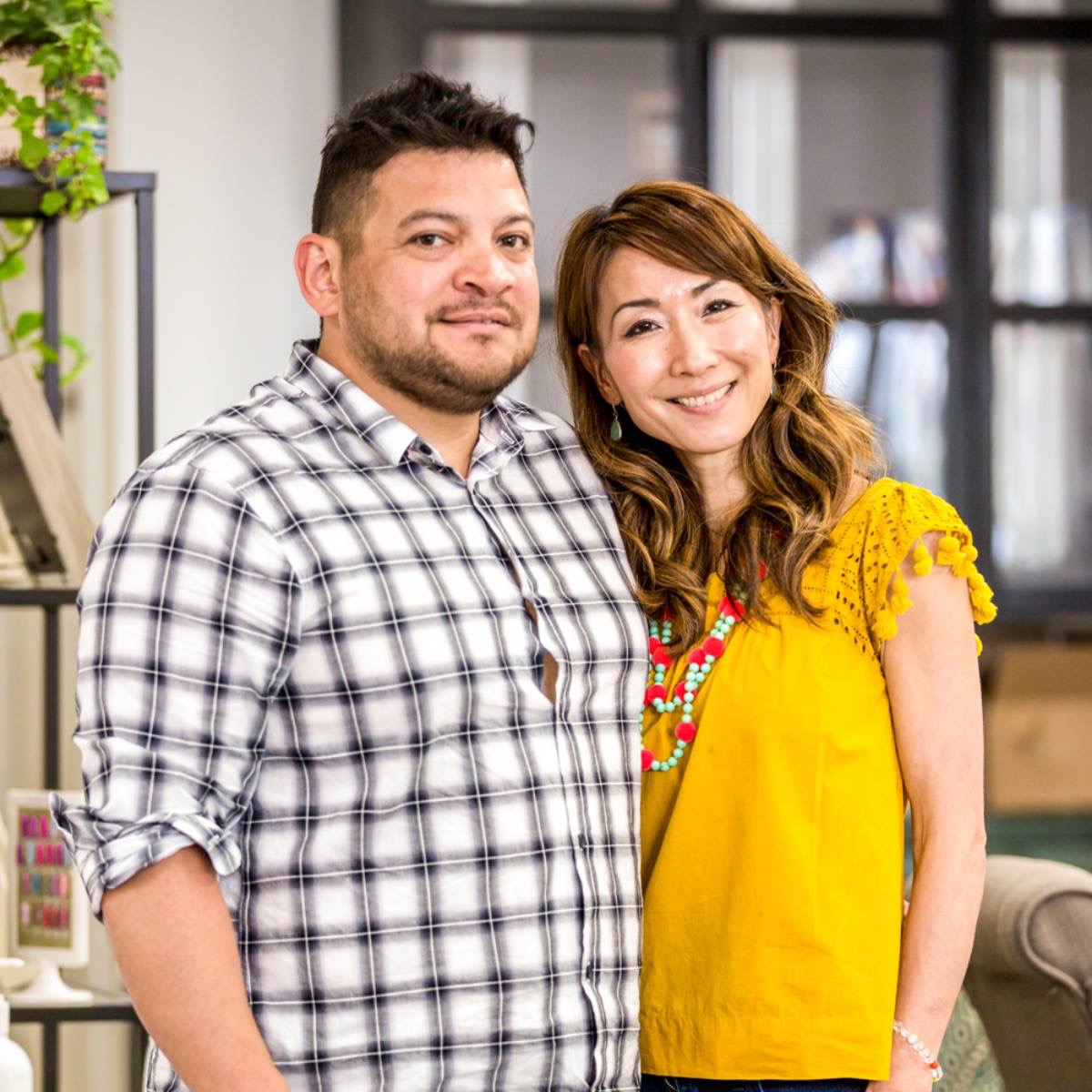A man and woman stand close together indoors, smiling at the camera, with a modern background. Word count: 20.