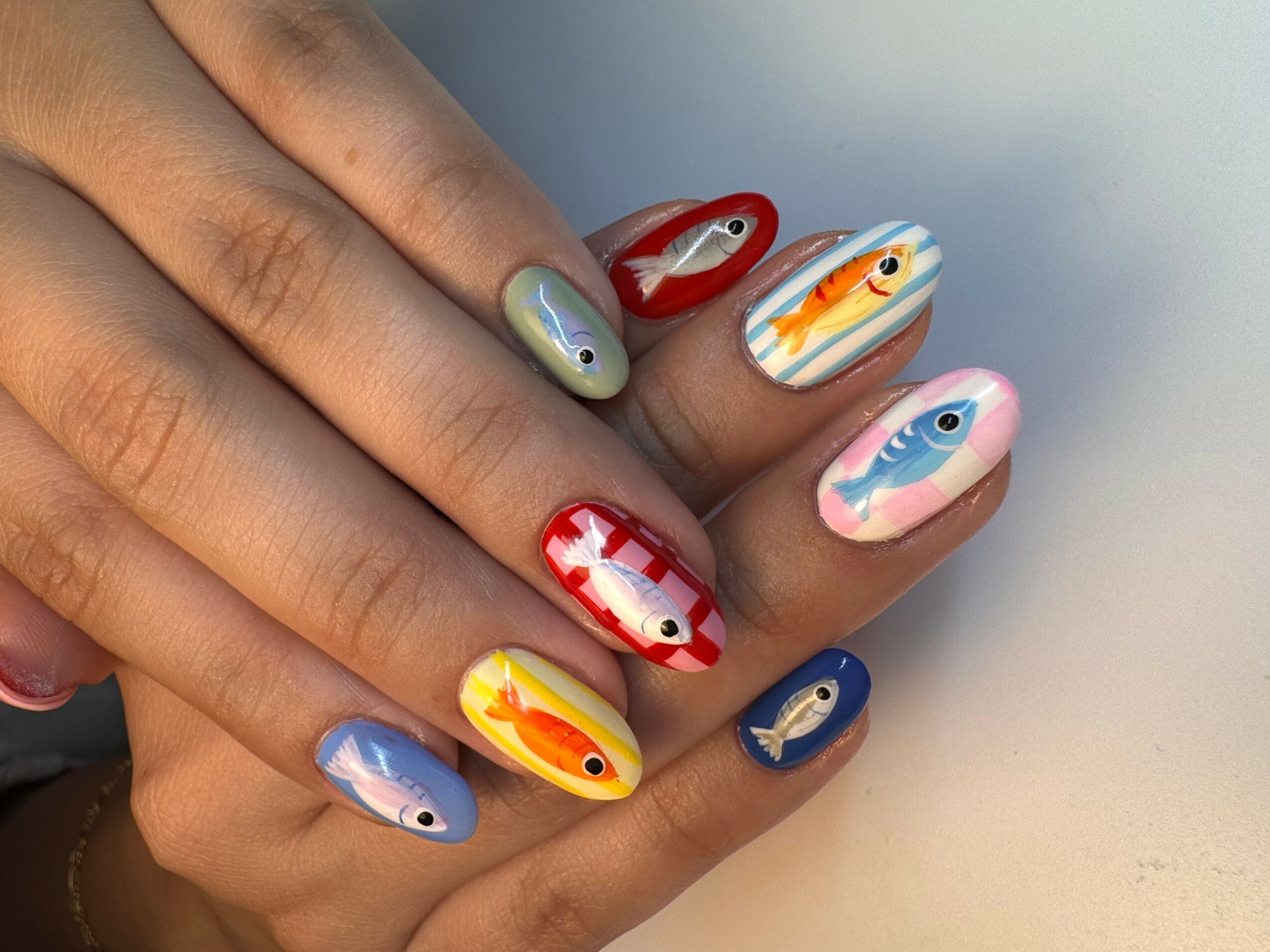 Hand with colorful fish-themed nail art on each fingernail, featuring various fish designs and colors.