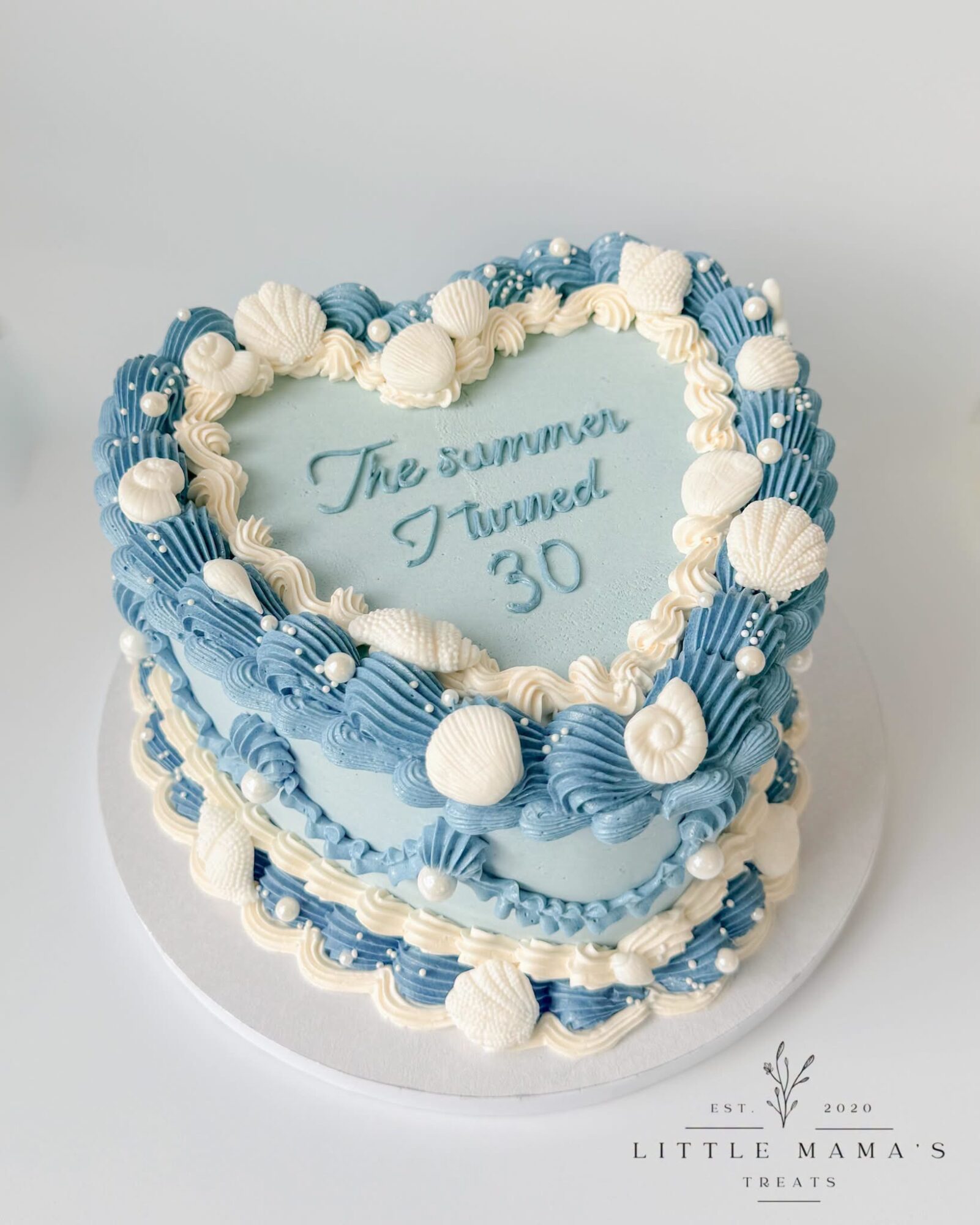Heart-shaped cake decorated with blue and white seashells and pearls, with a message inside reading 'The summer I turned 30'.