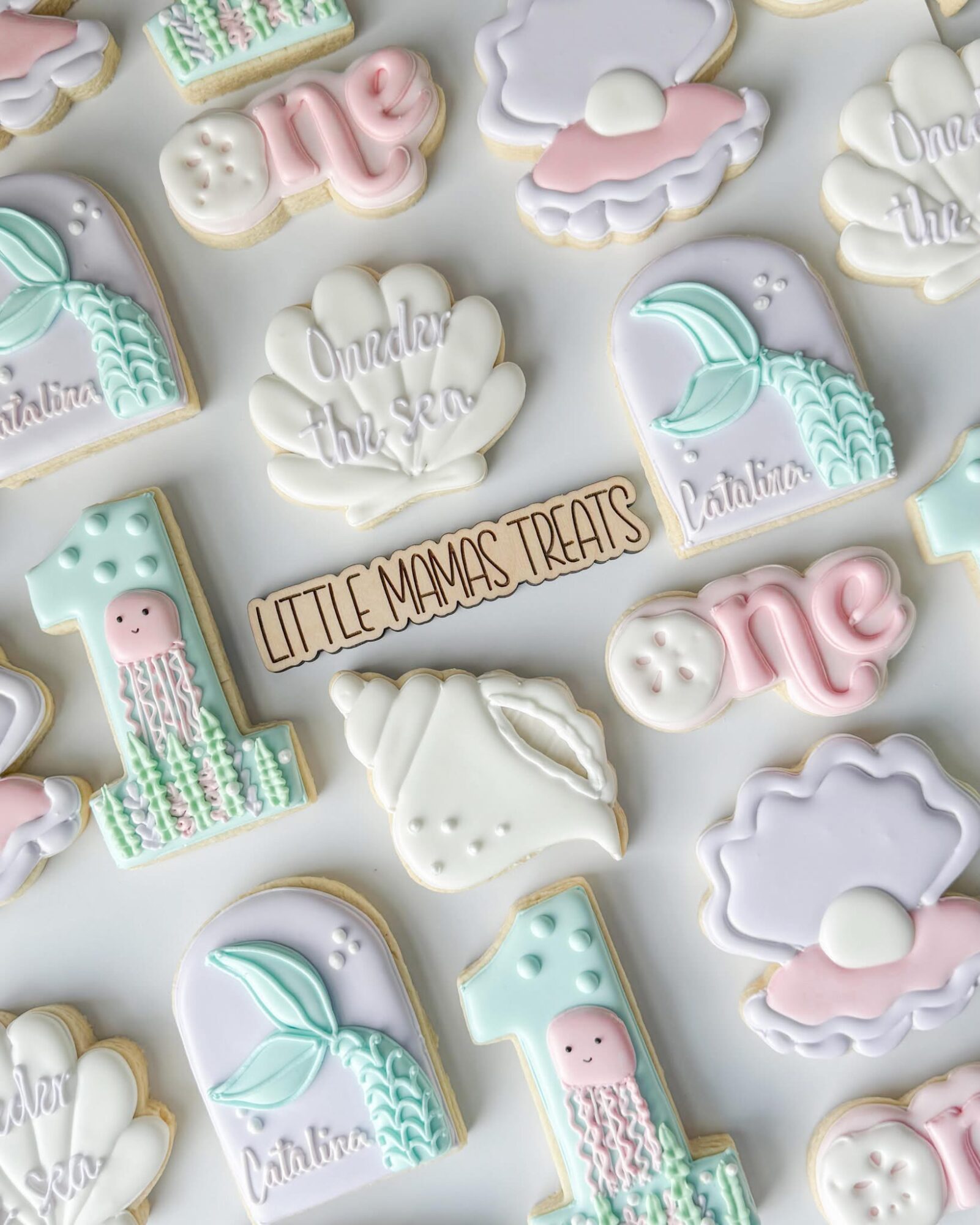 Assorted pastel-colored cookies with baby shower themes, including ones with the number one, clouds, and a whale, on a white background.