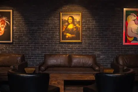 Art gallery with three paintings on a dark brick wall, leather sofas, and chairs in a cozy setting.