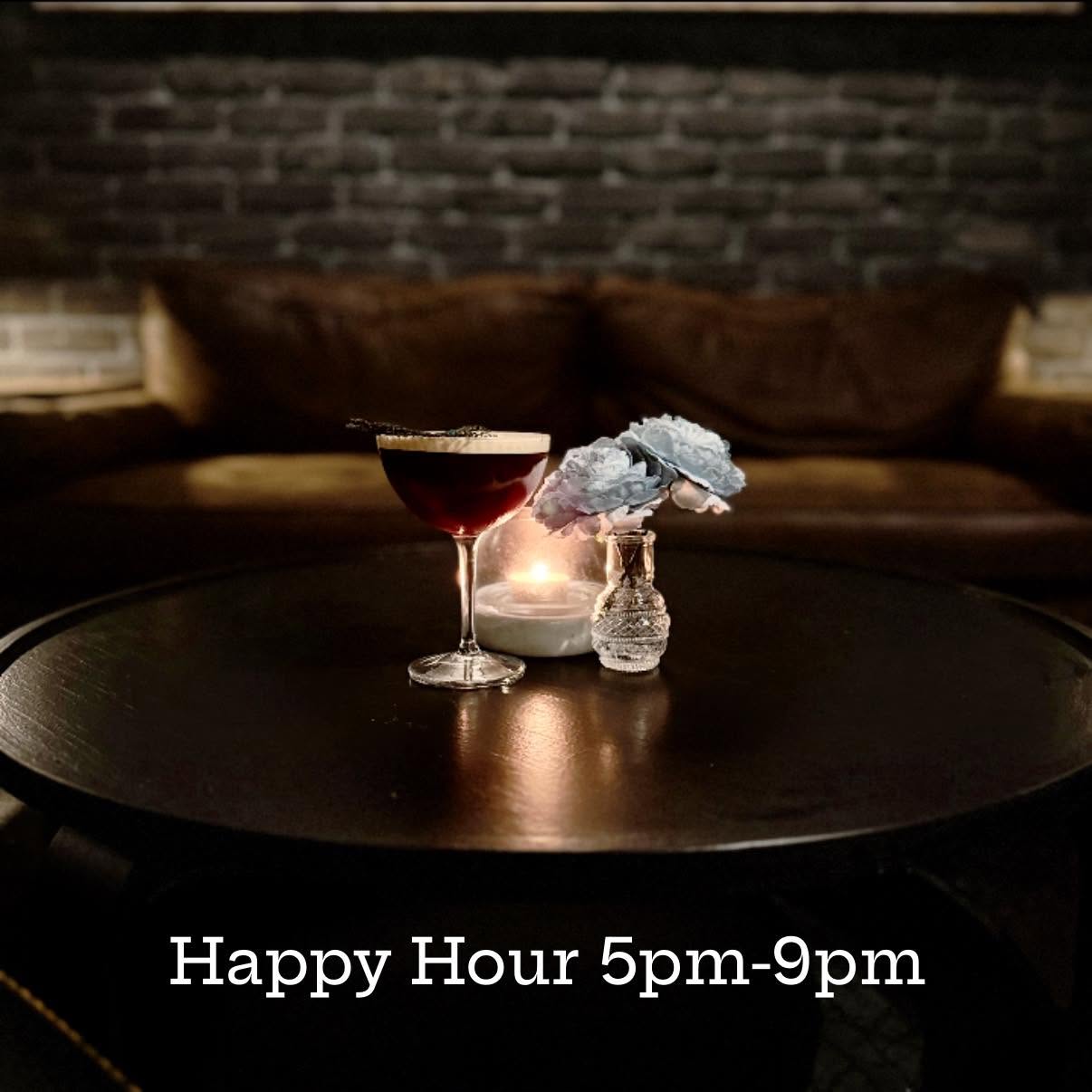 A dark table with a cocktail glass, a small sculpture, and a candle in a dimly lit room with a brick wall background.