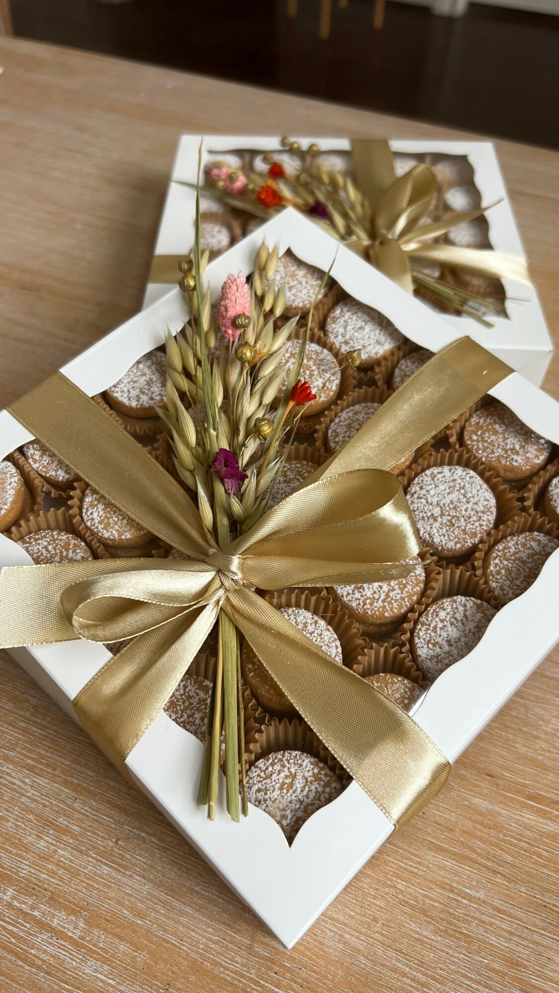 Open box of chocolates decorated with a gold ribbon and small pink flowers, on a wooden surface.