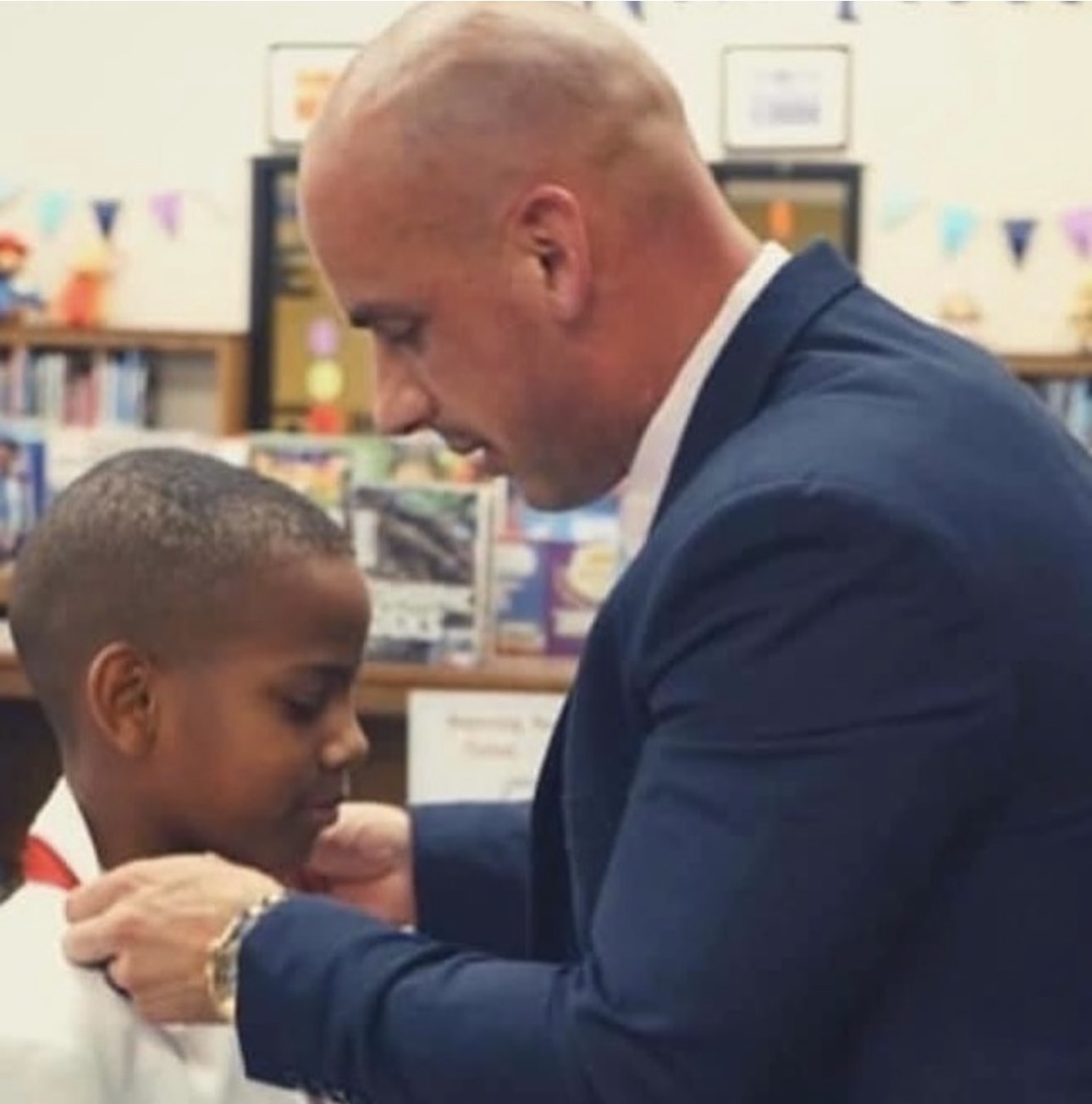 Adult man and child in a library, facing each other, with bookshelves in the background.