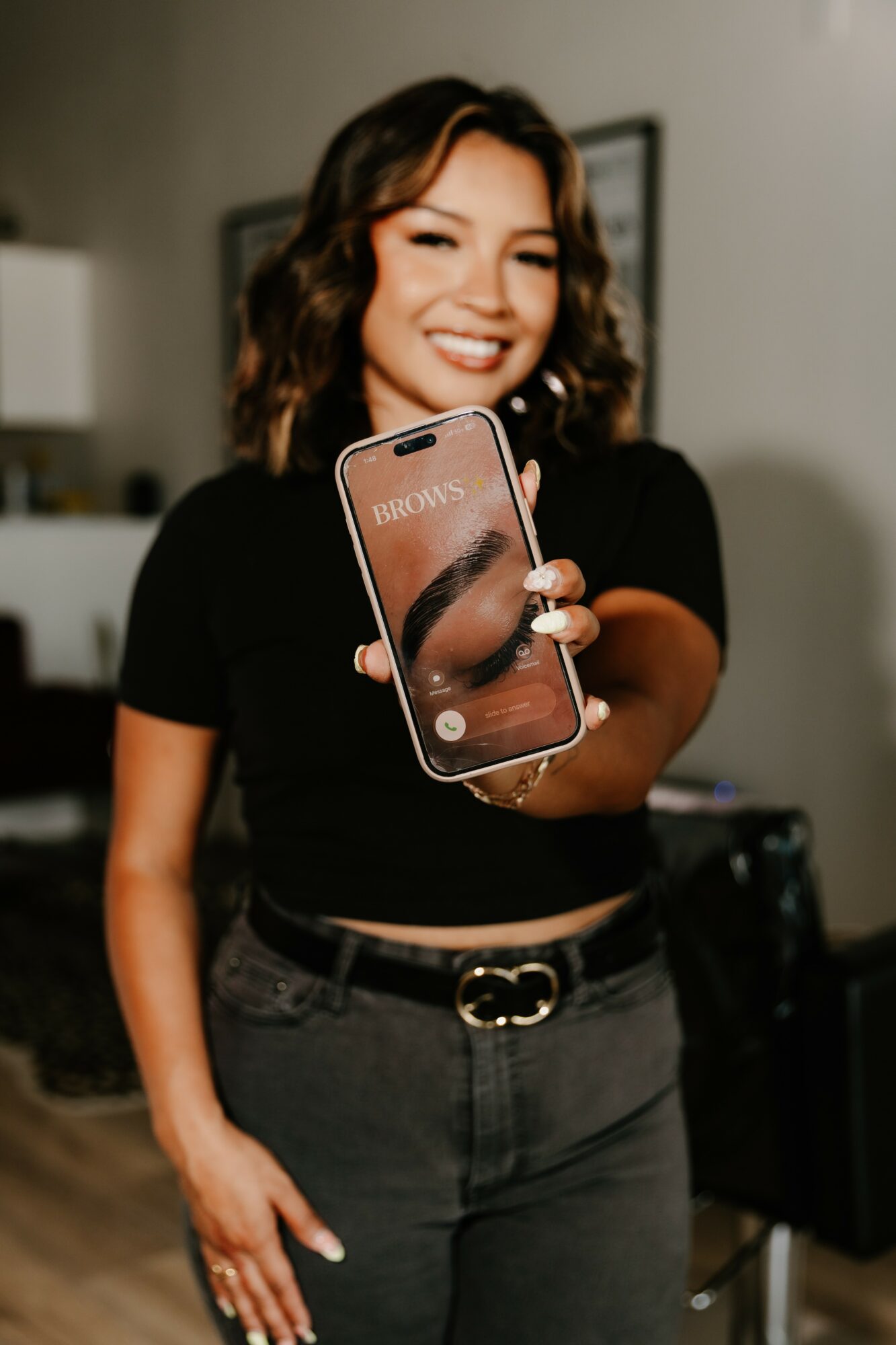 Woman smiling and holding a smartphone towards the camera in an indoor setting.