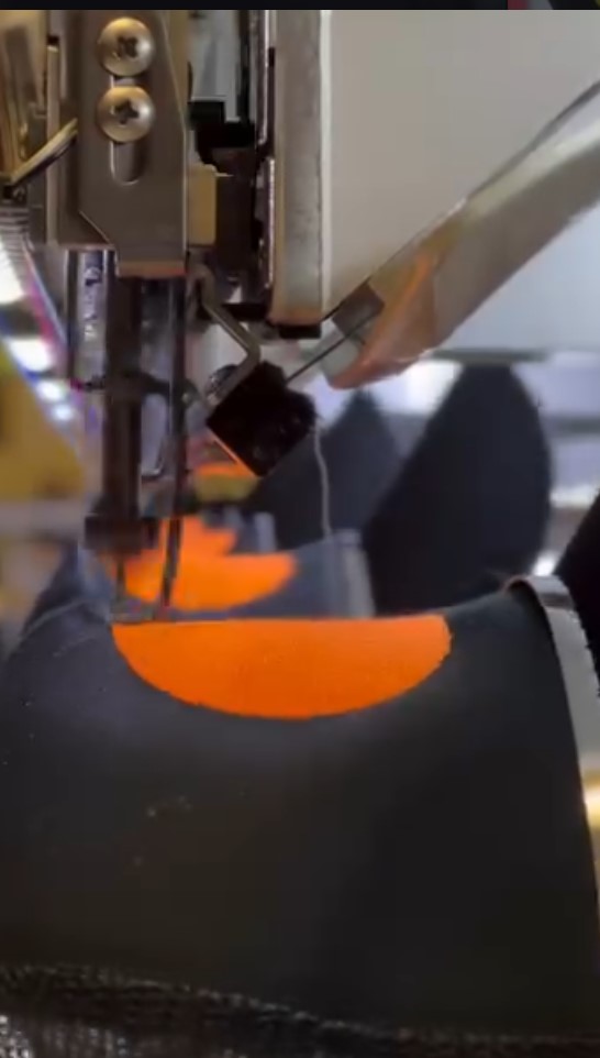 Close-up of a manufacturing process with machinery and a black object with orange markings being handled.