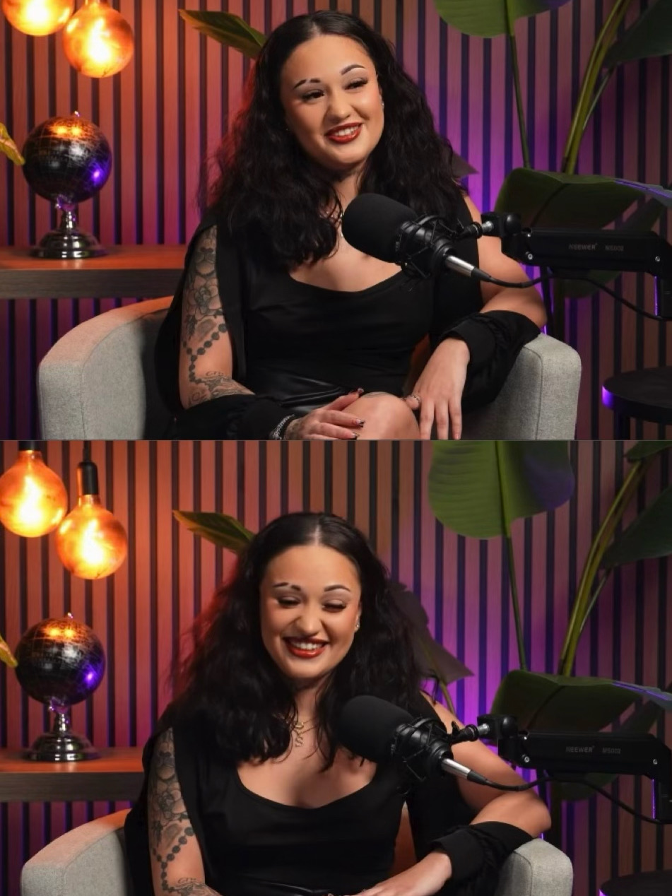 Woman with long dark hair smiling, sitting on a sofa with a microphone, in a colorful studio setting.