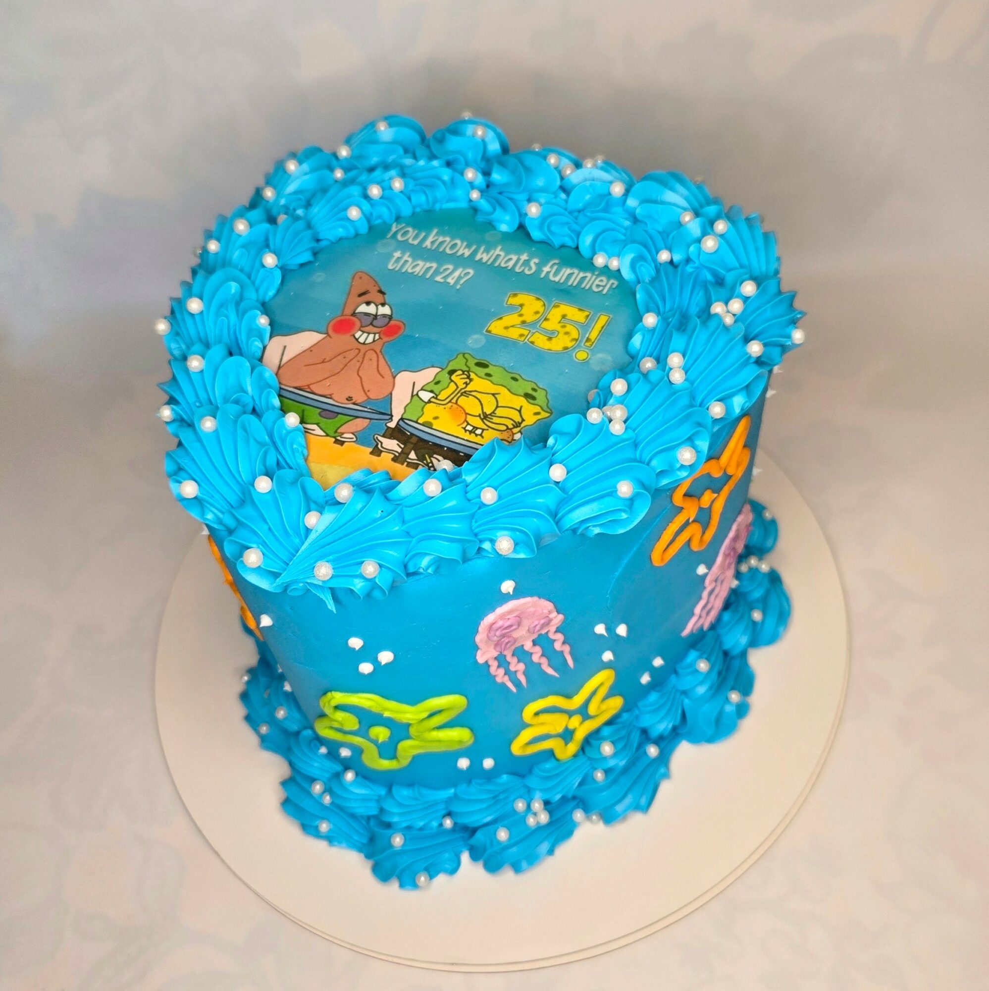 Blue birthday cake with SpongeBob SquarePants theme, decorated with blue frosting, jellyfish, and character images, on a white surface.
