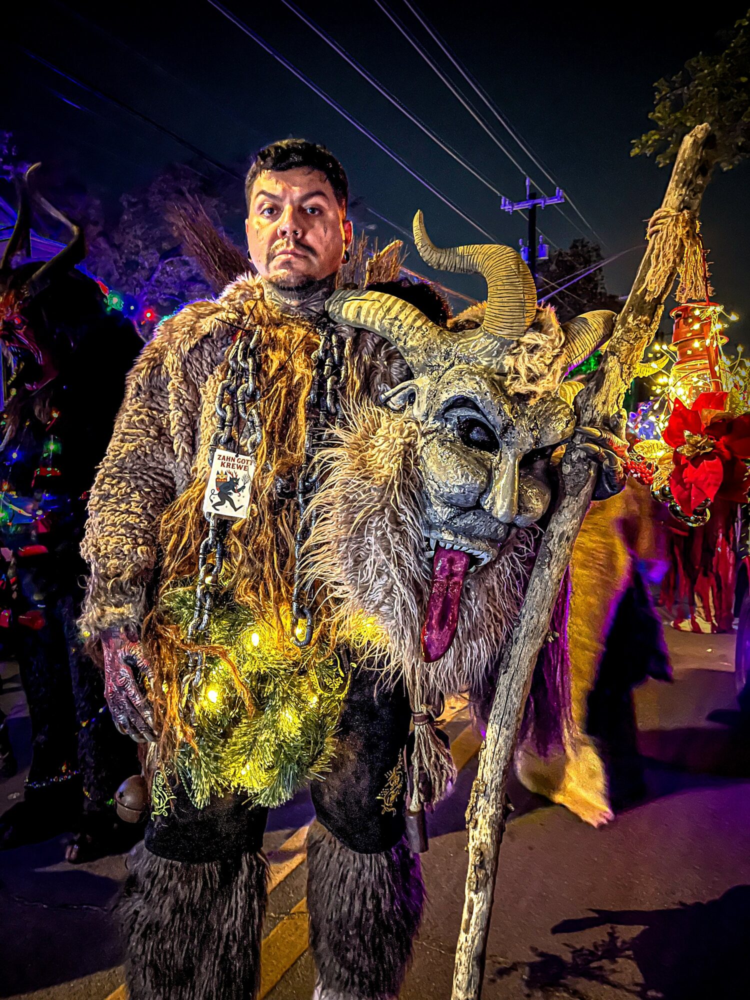 Person in elaborate costume with a large, decorated mask resembling a mythical creature, at night with colorful lights.