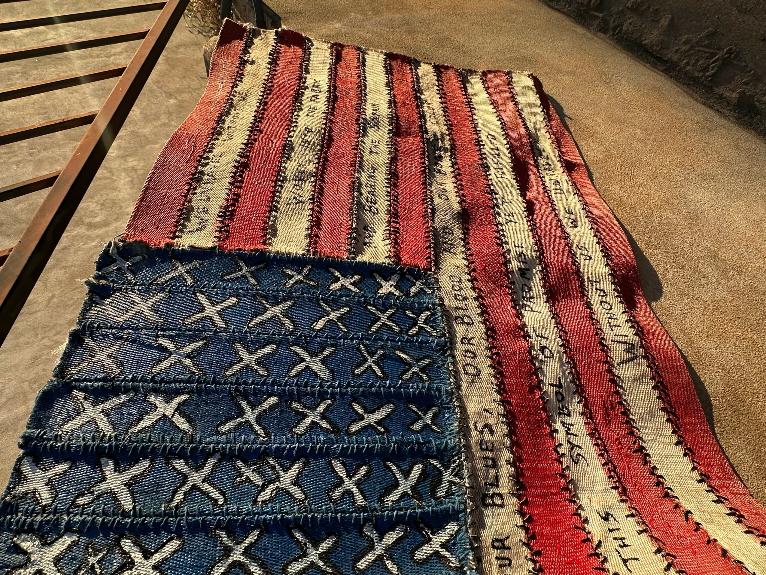 Two woven rugs with red, white, and beige stripes and a blue rug with white X patterns, laid on a floor.