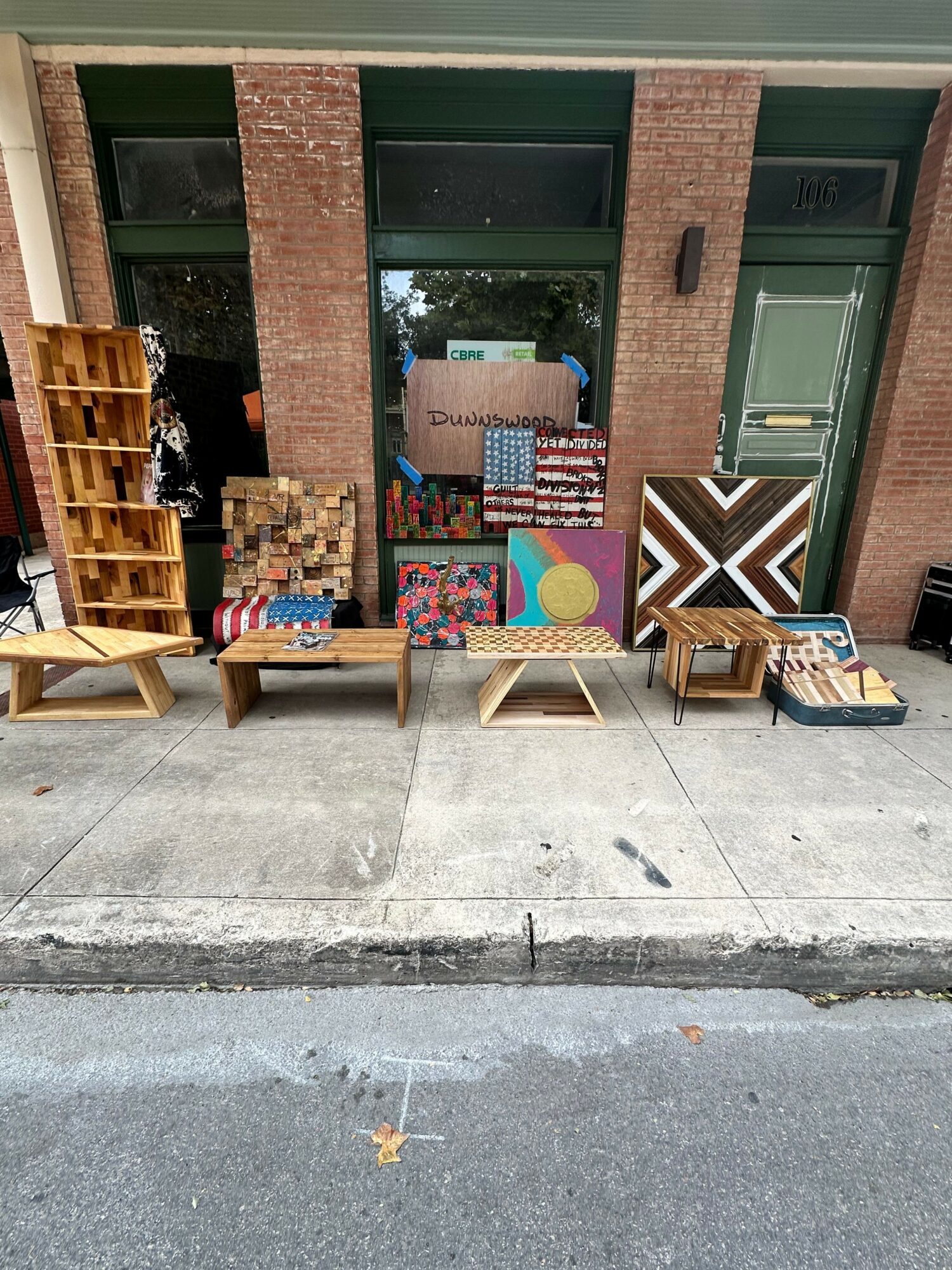 Outdoor display with furniture, artwork, and decorations against a brick building, on a sidewalk.