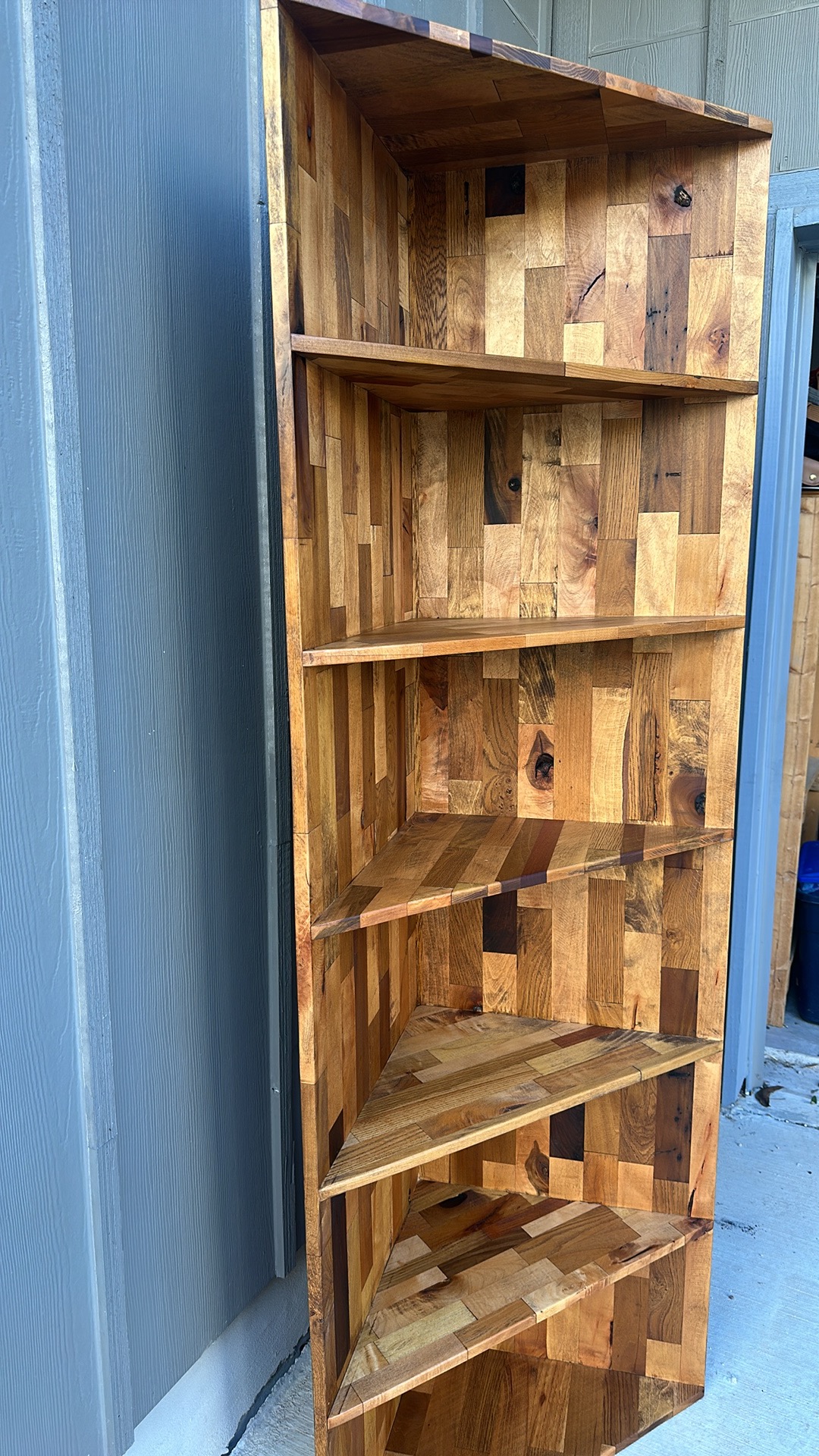 Tall wooden bookshelf with five shelves, leaning against a wall outdoors.