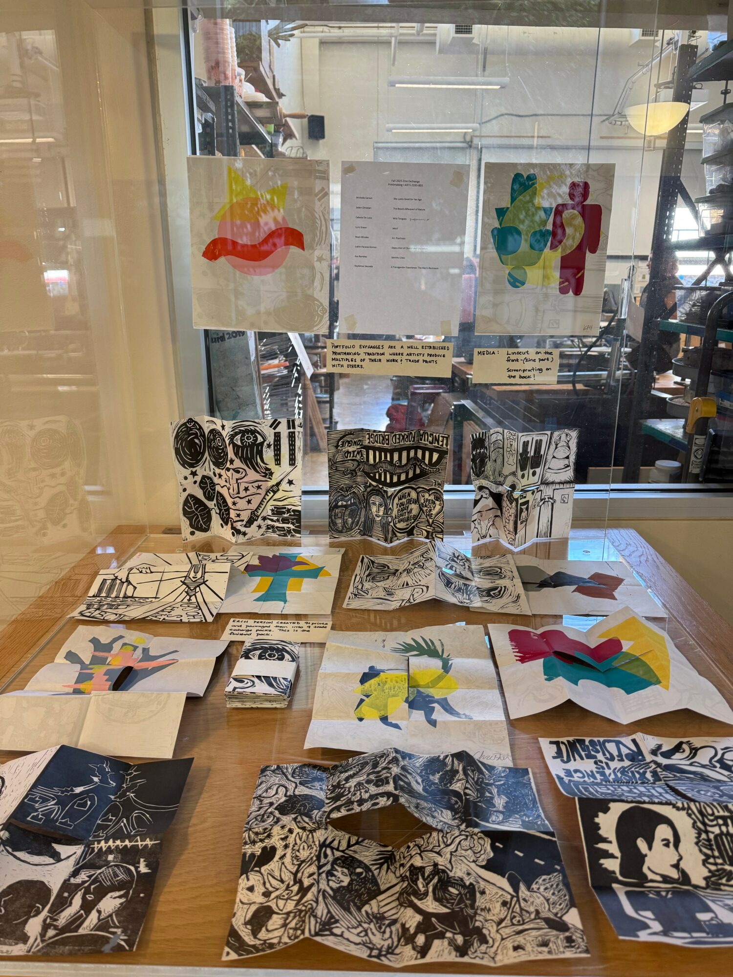 Display of colorful artwork and photographs on a table with a glass window background.