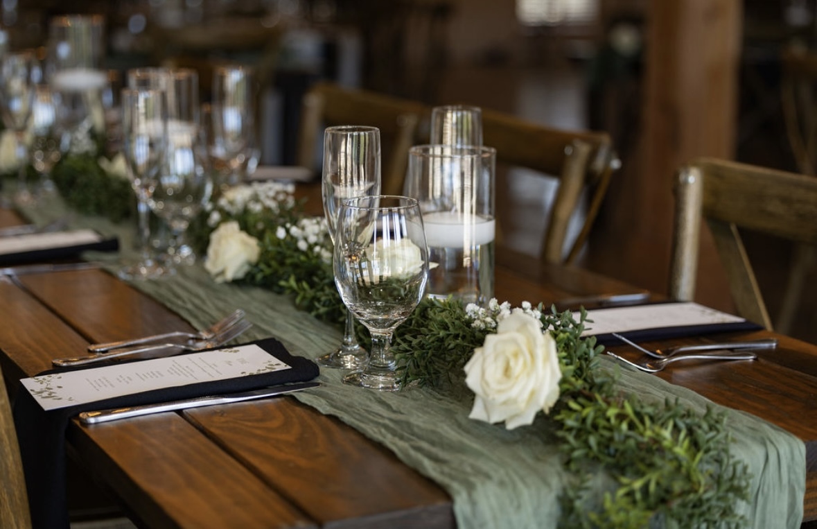 Table decorated with a green runner, white flowers, and glassware, set for a formal event or celebration.